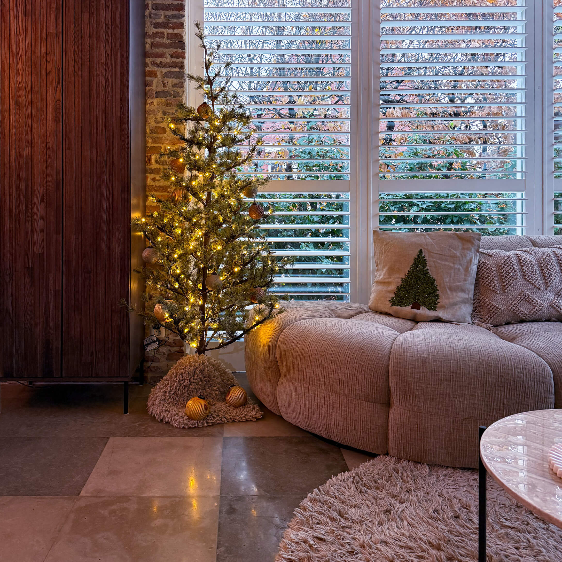 Gezellige woonkamer met beige bank, kussen met kerstboom en verlichte LED-decoratieve kerstboom