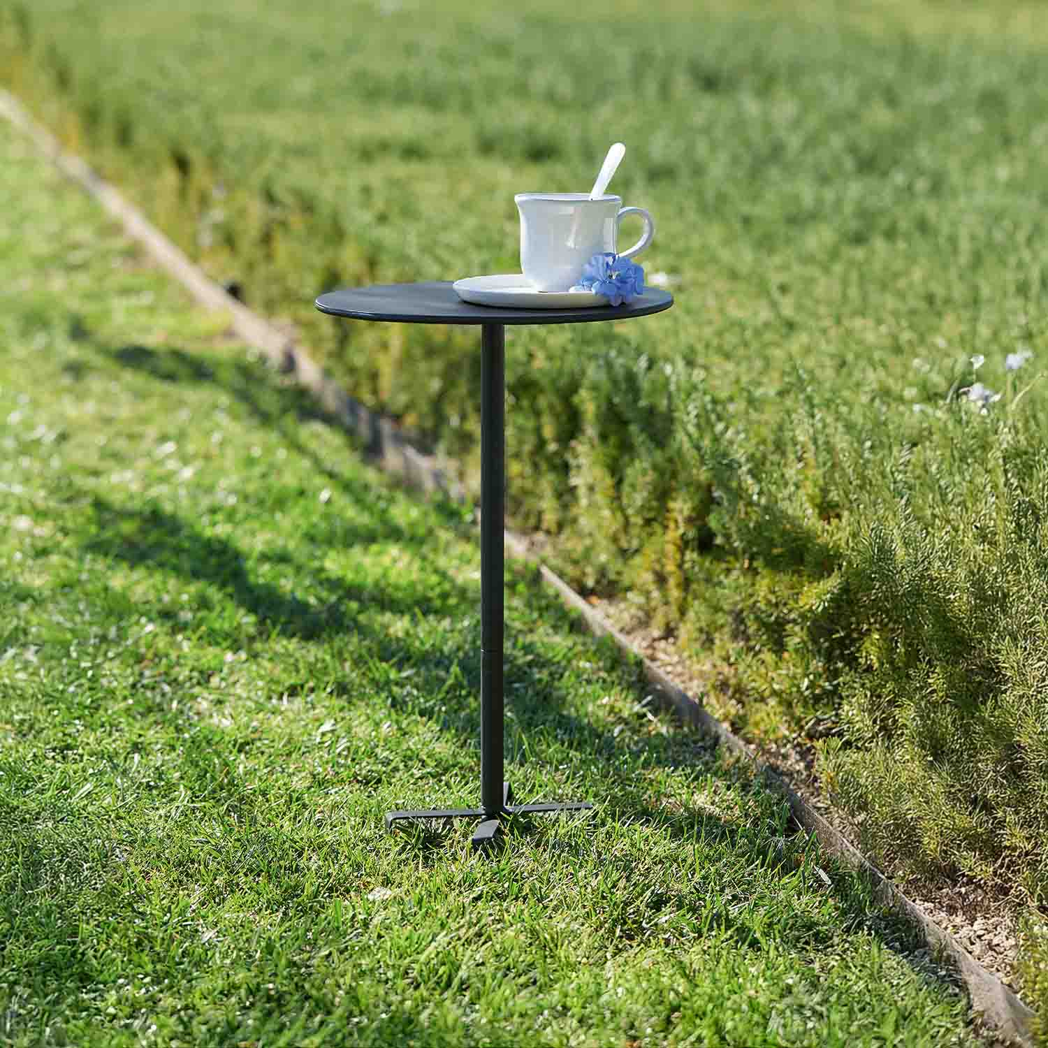 Kleine zwarte metalen tuintafel met witte mok en blauwe bloem op gras