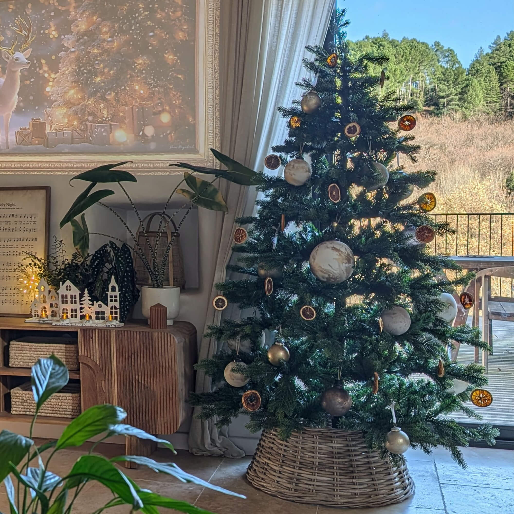 Kerstboom met natuurlijke versieringen en rieten standaard in gezellige woonkamer met uitzicht op bos