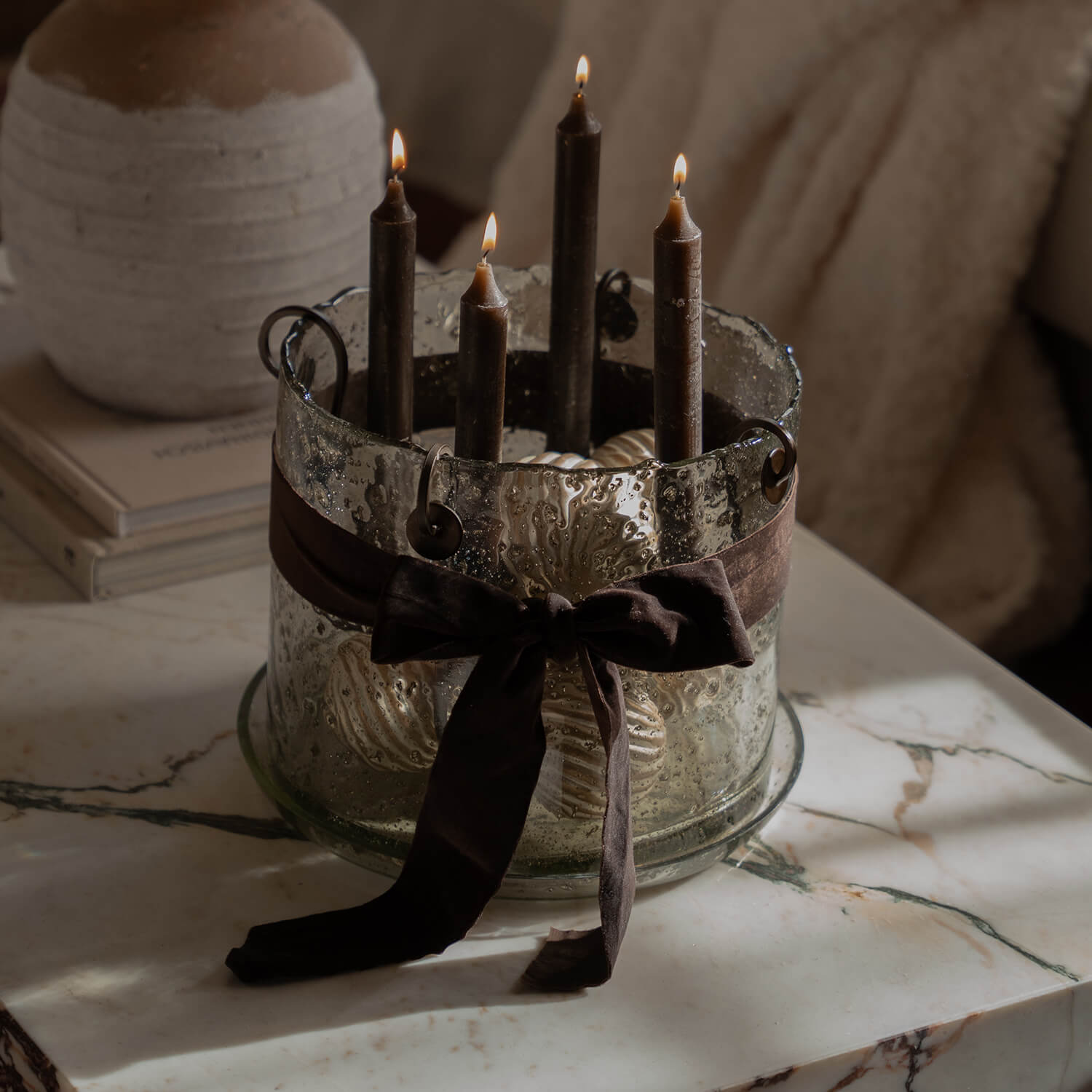 Glazen kandelaar met vier bruine kaarsen en decoratieve strik op een marmeren tafel