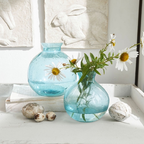 Transparante blauwe glazen vazen met madeliefjes, natuurlijke tafeldecoratie