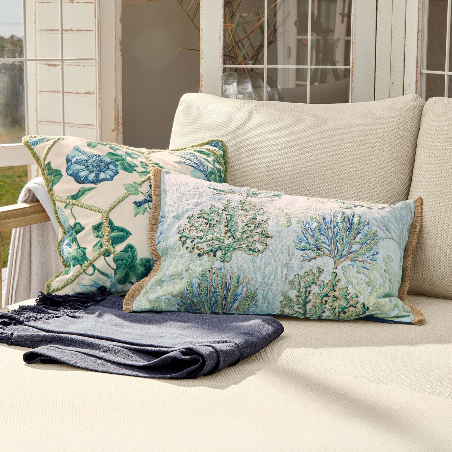 Kussenhoes set van 2 Ambrisse Tweekleurige decoratieve kussens met plantenmotief op crèmekleurige bank met donkerblauwe deken