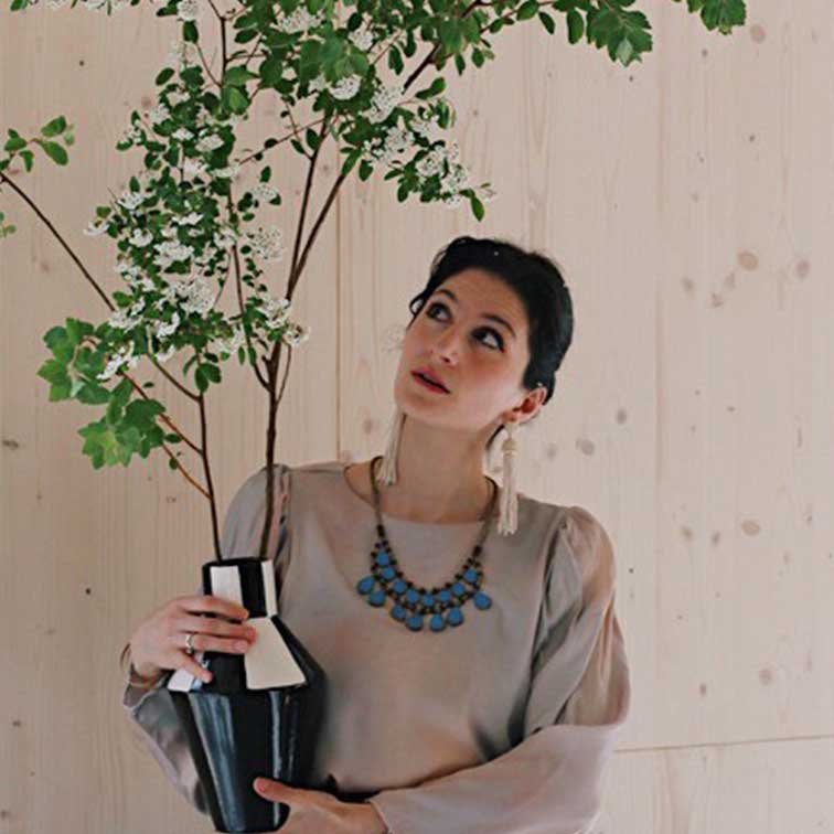 Vrouw houdt zwart-witte keramische vaas met groene takken voor lichte houten achtergrond
