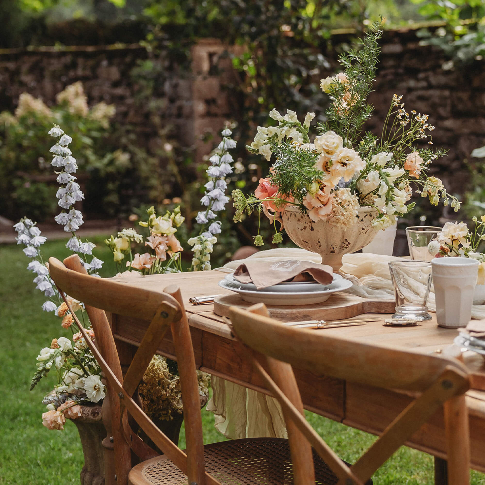 Houten tuintafel met bloemstuk en natuurlijke stoelen op groen gras