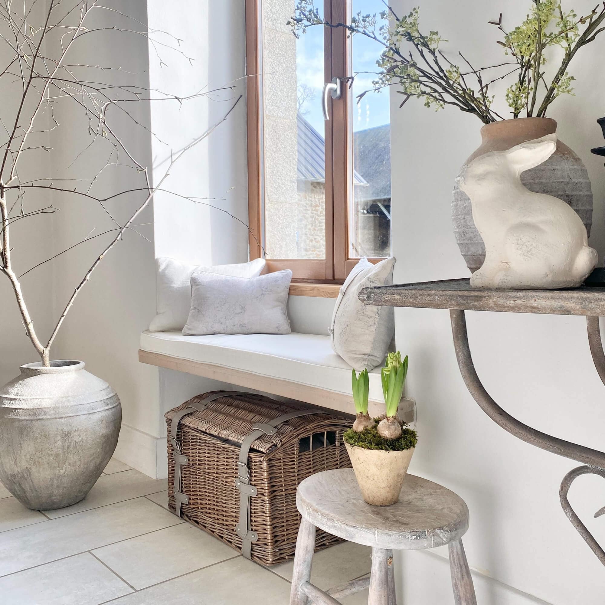 Gezellige hoek met witte kussens, rieten kist en konijnendecoratie in lichte kamer