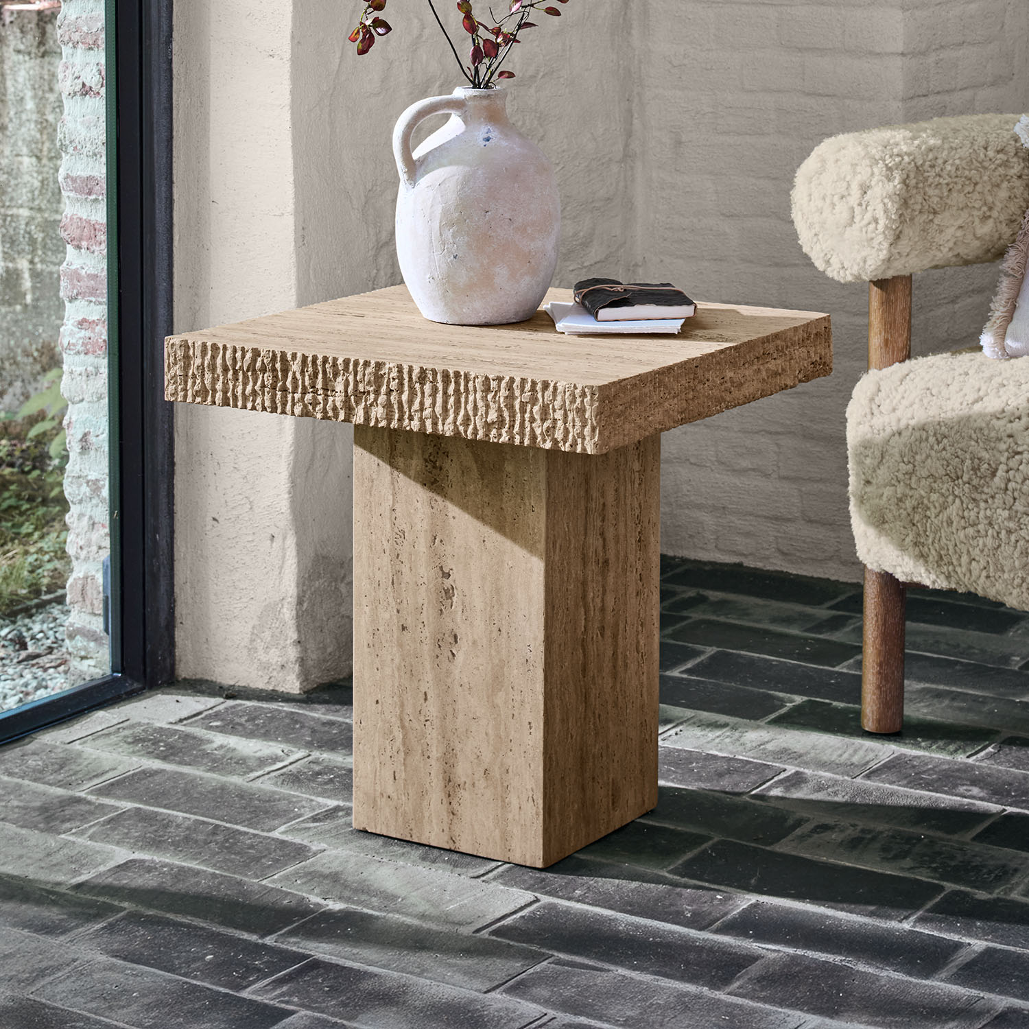 Vierkante bijzettafel van beige travertijn met decoratieve vaas en boeken erop
