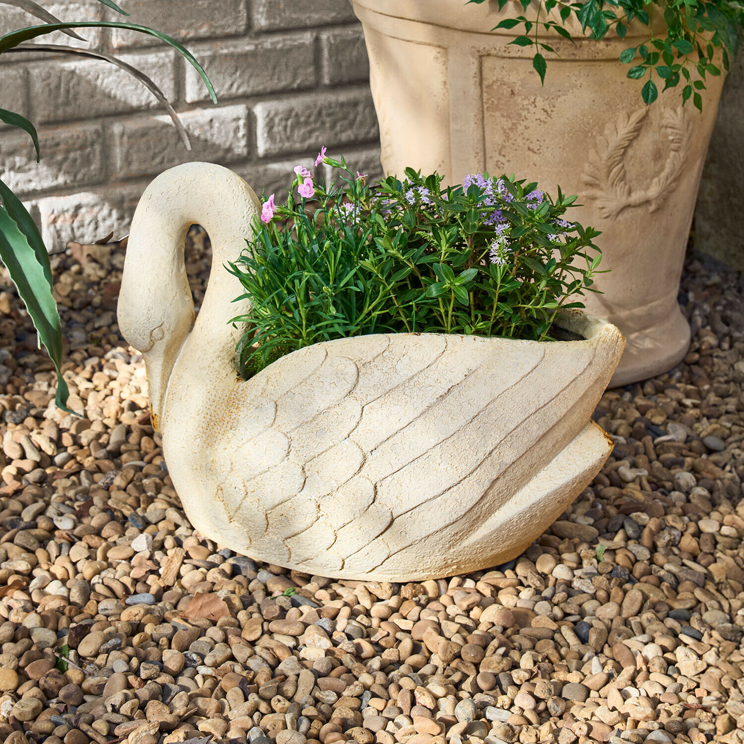 Zwanenvormige bloempot van licht steen met groene en paarse planten op kiezelstenen
