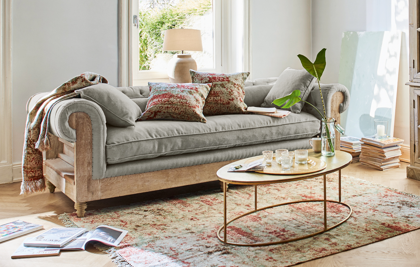Grijze bank met houten frame en oosterse vloerkleed in lichte woonkamer met decoratieve kussens