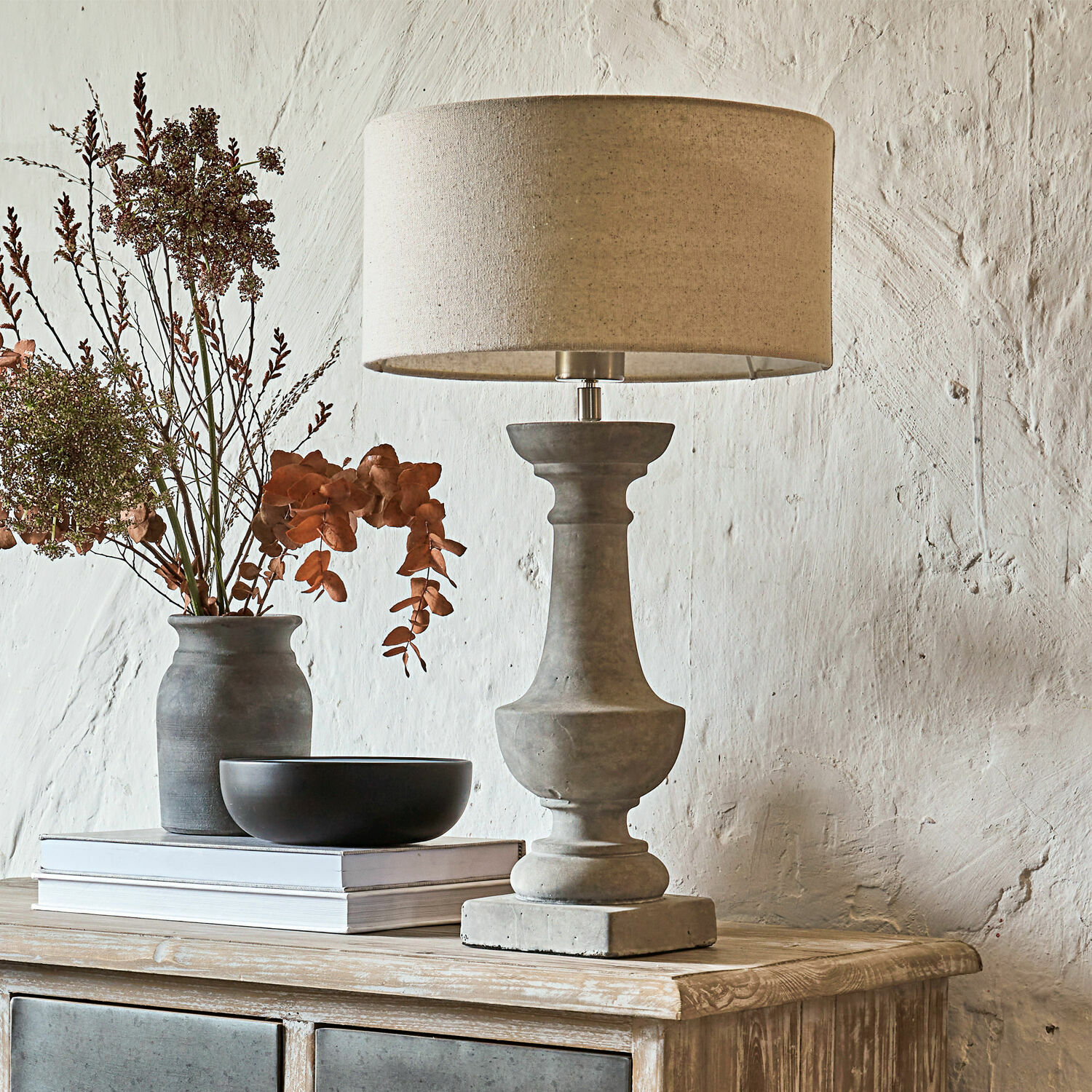 Betonnen tafellamp met beige kap op houten dressoir met decoratie