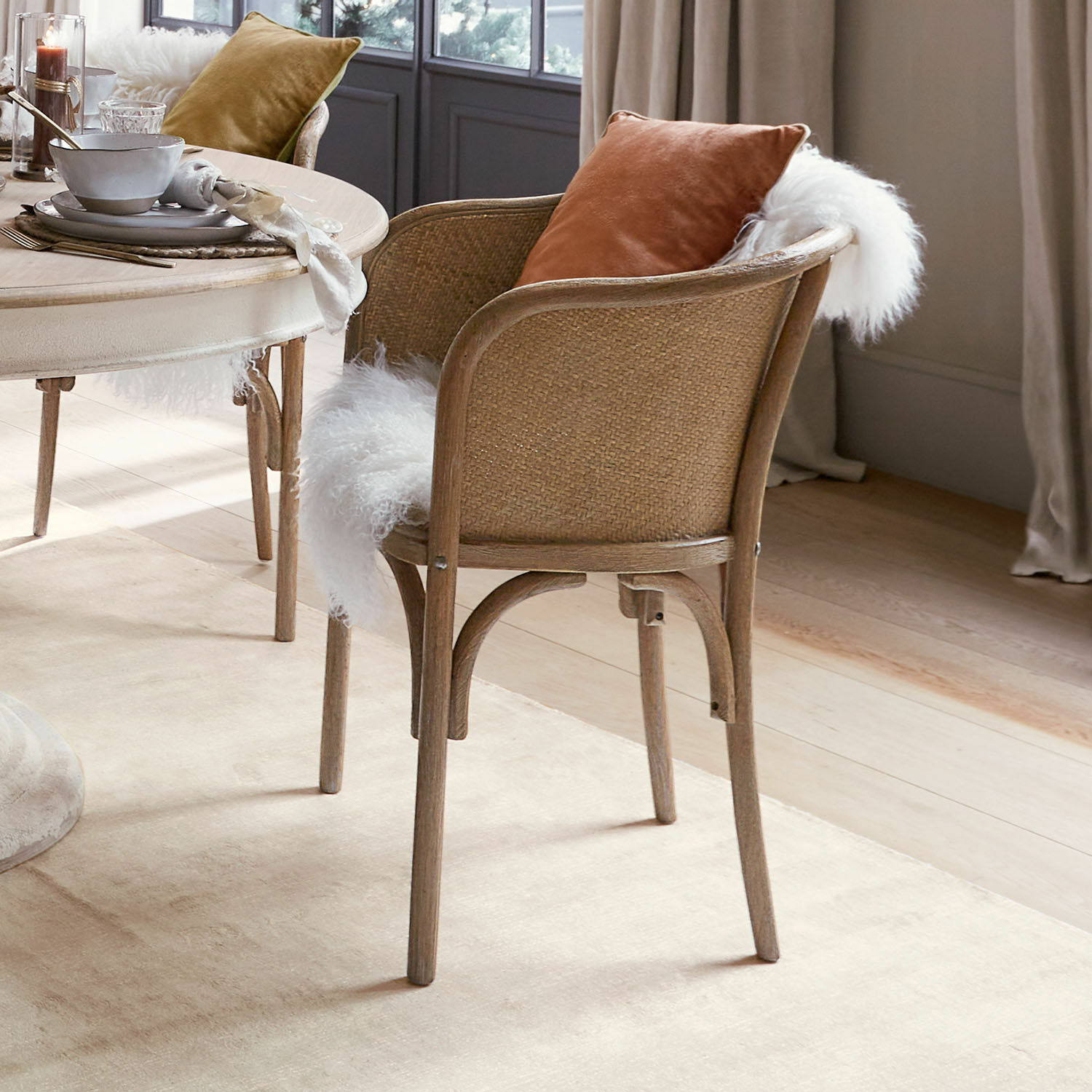 Stoel van hout en riet met witte bont en oranje kussen in een gezellige eetkamer