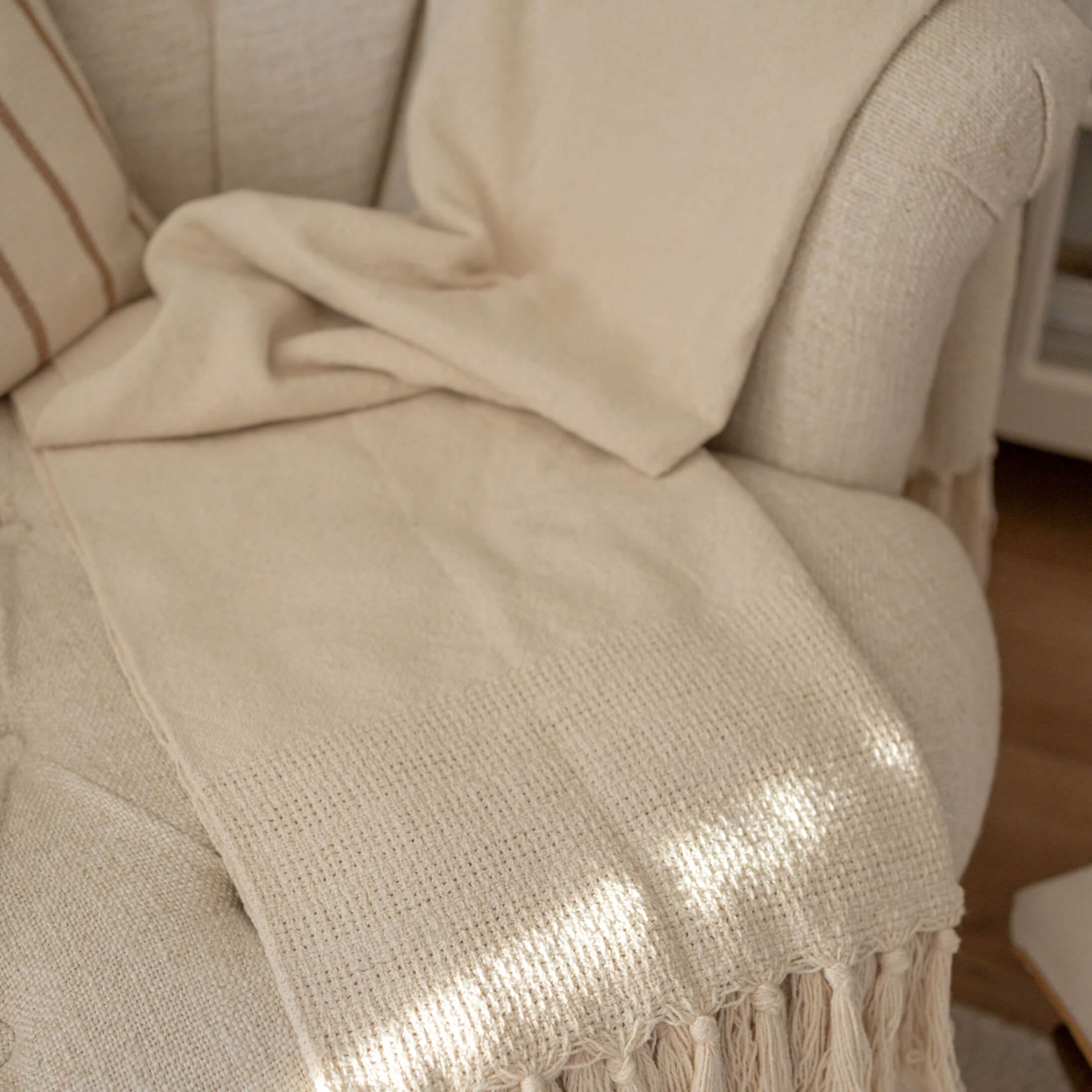 Beige deken met franjes op lichte stoel, zachte stof voor interieurdecoratie en comfort