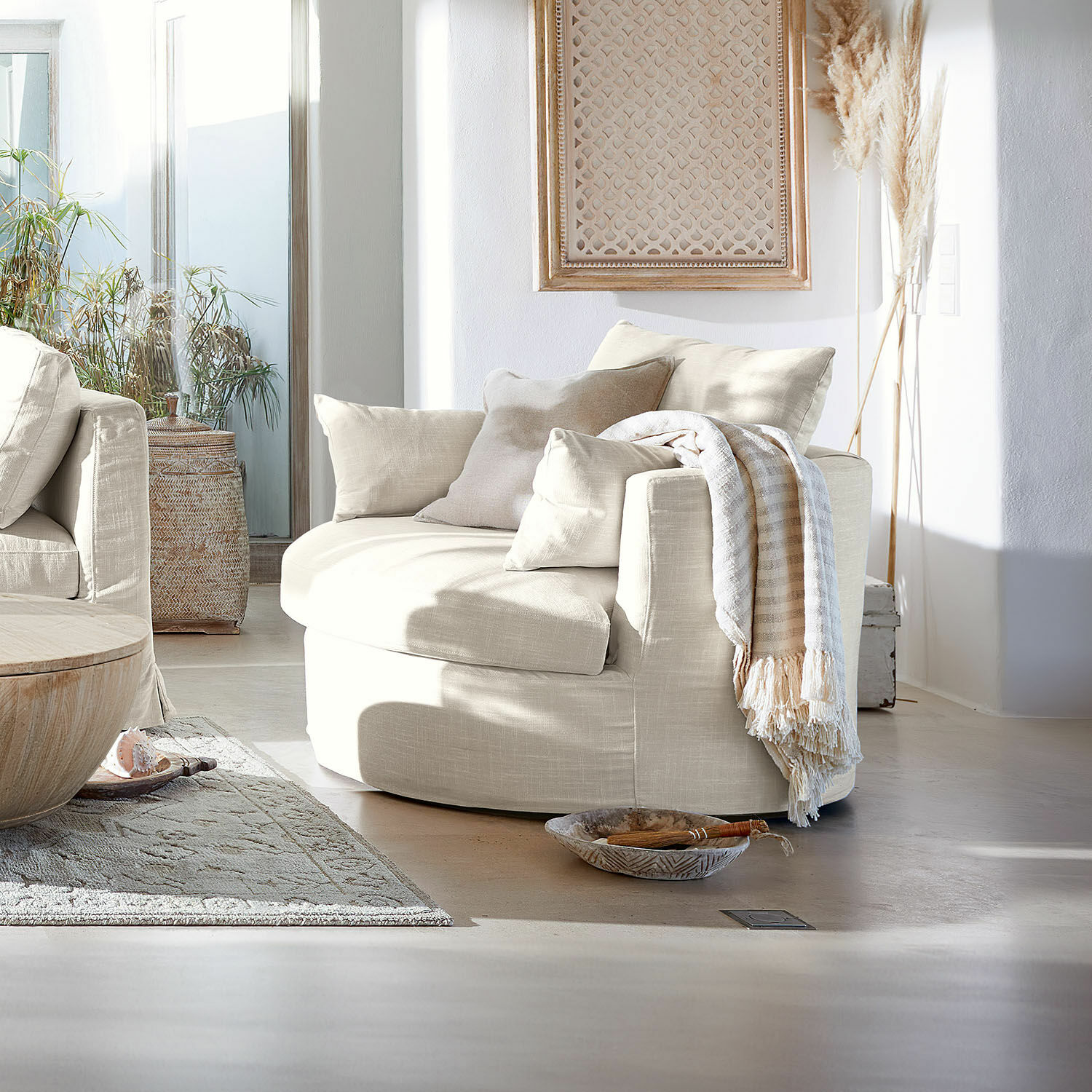 Draaifauteuil Beige ronde stoffen fauteuil met kussens en plaid in lichte woonkamer met natuurlijk licht