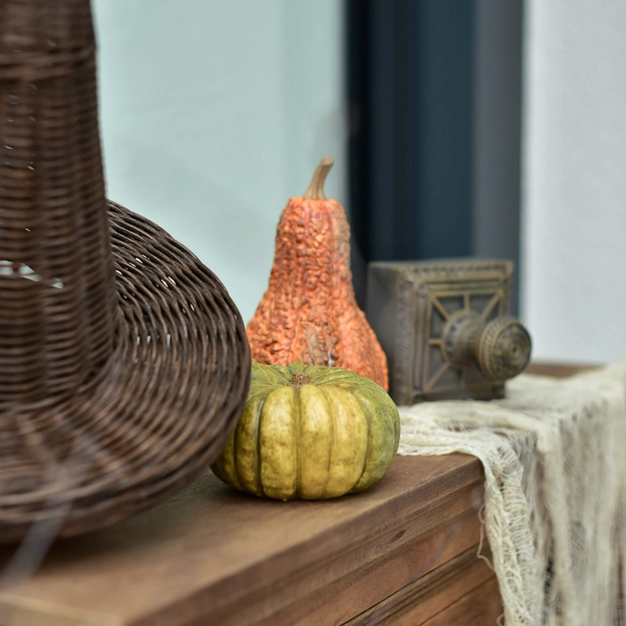 Decoratieve groene en oranje pompoenen op een houten blad naast een rieten mand