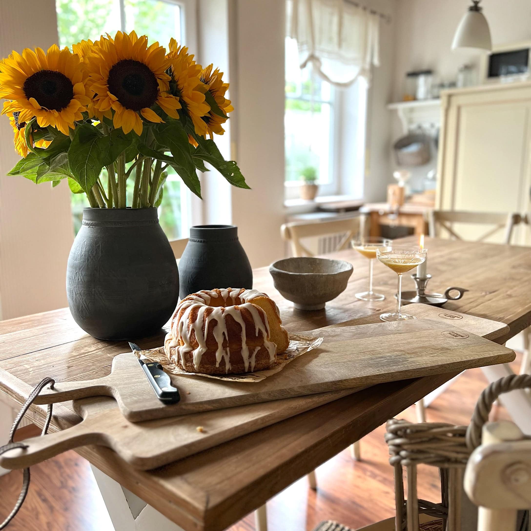 Houten snijplank met cake en zwarte vaas met gele zonnebloemen op houten keukentafel