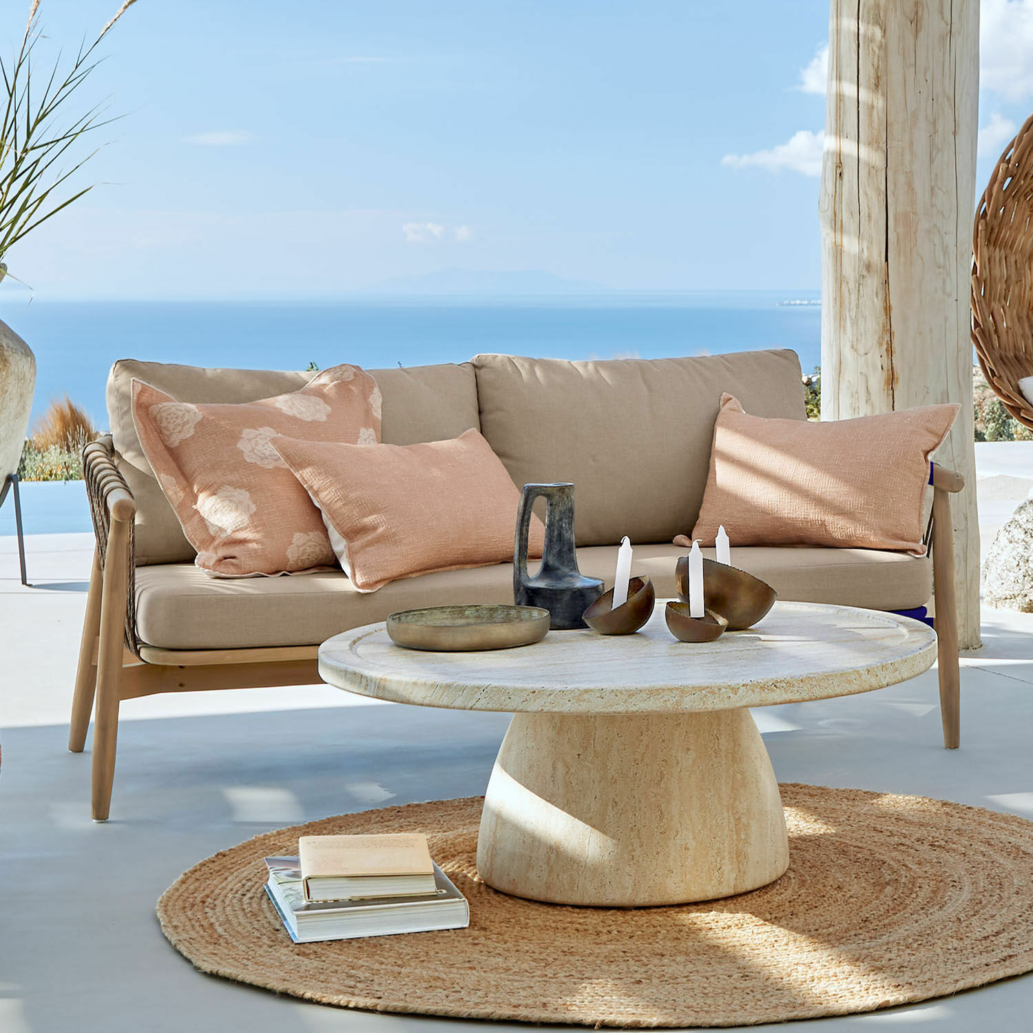 Beige bank met kussens en ronde stenen tafel op terras met zeezicht