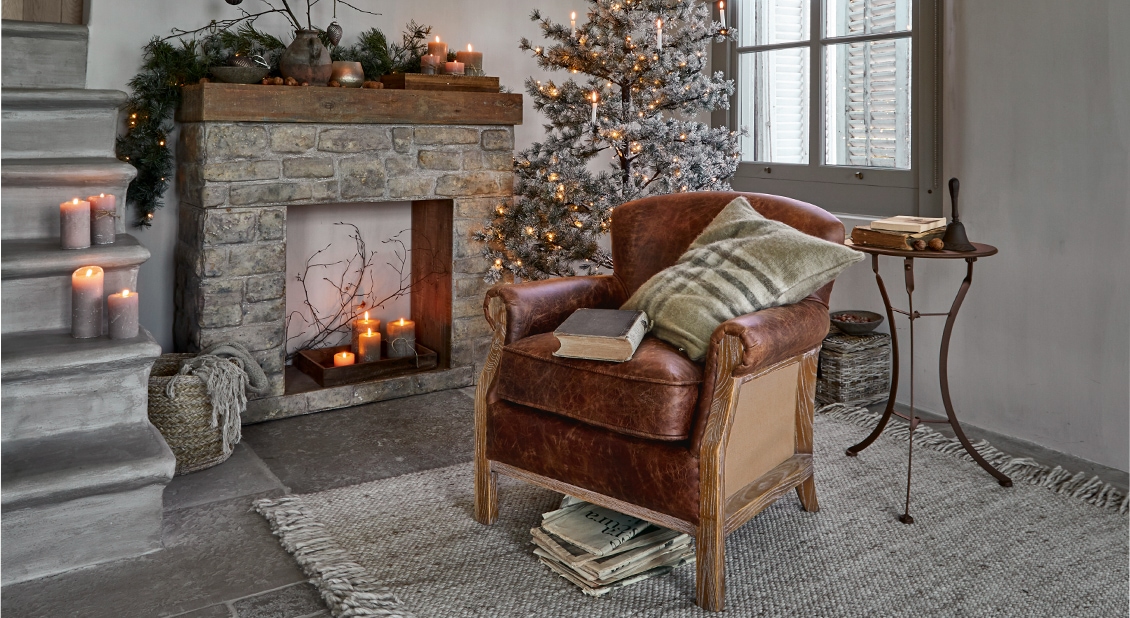 Gezellige woonkamer met bruine leren fauteuil, stenen open haard en kerstdecoratie met boom en kaarsen