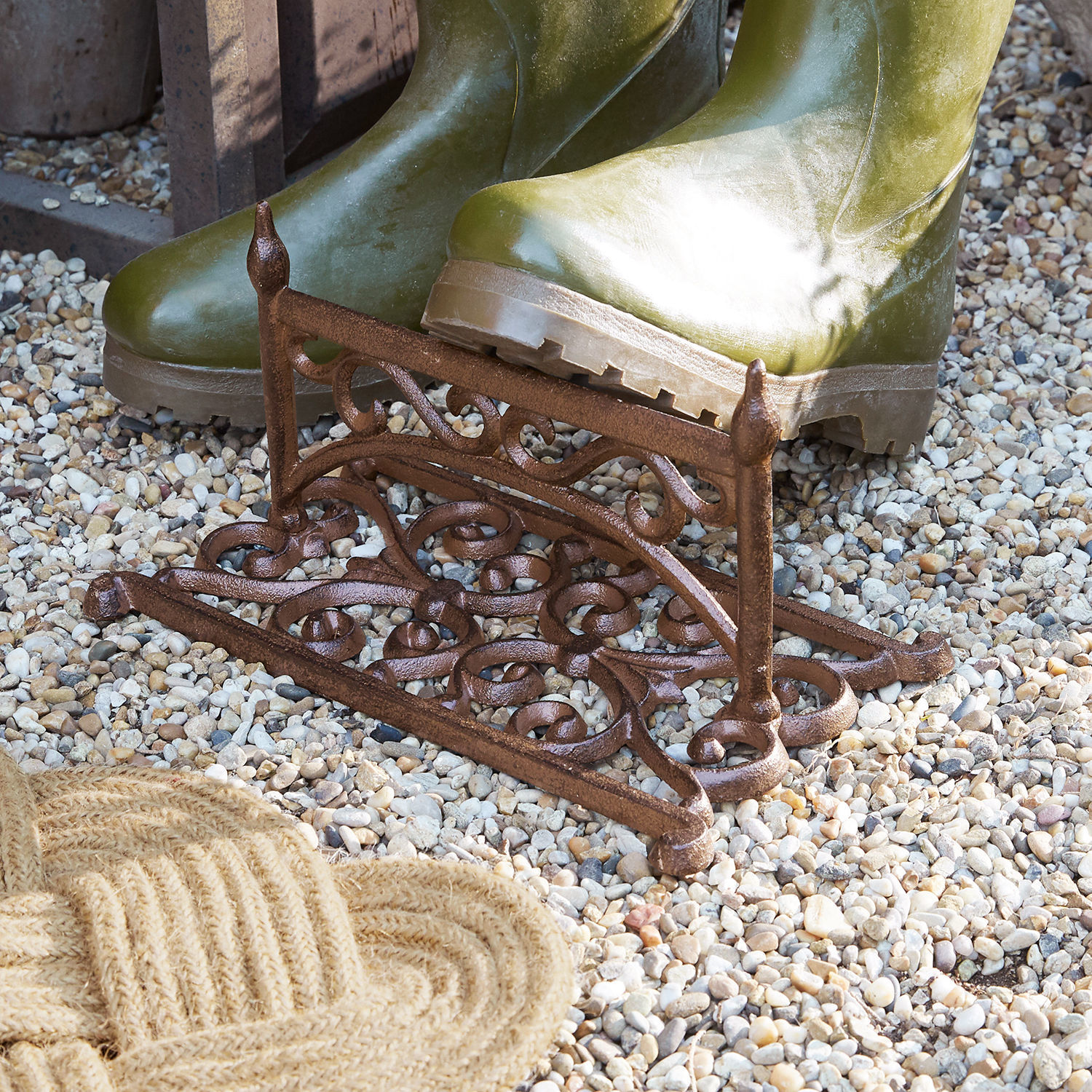 Bruine gietijzeren deurmat met decoratief patroon op grind, groene laarzen erop