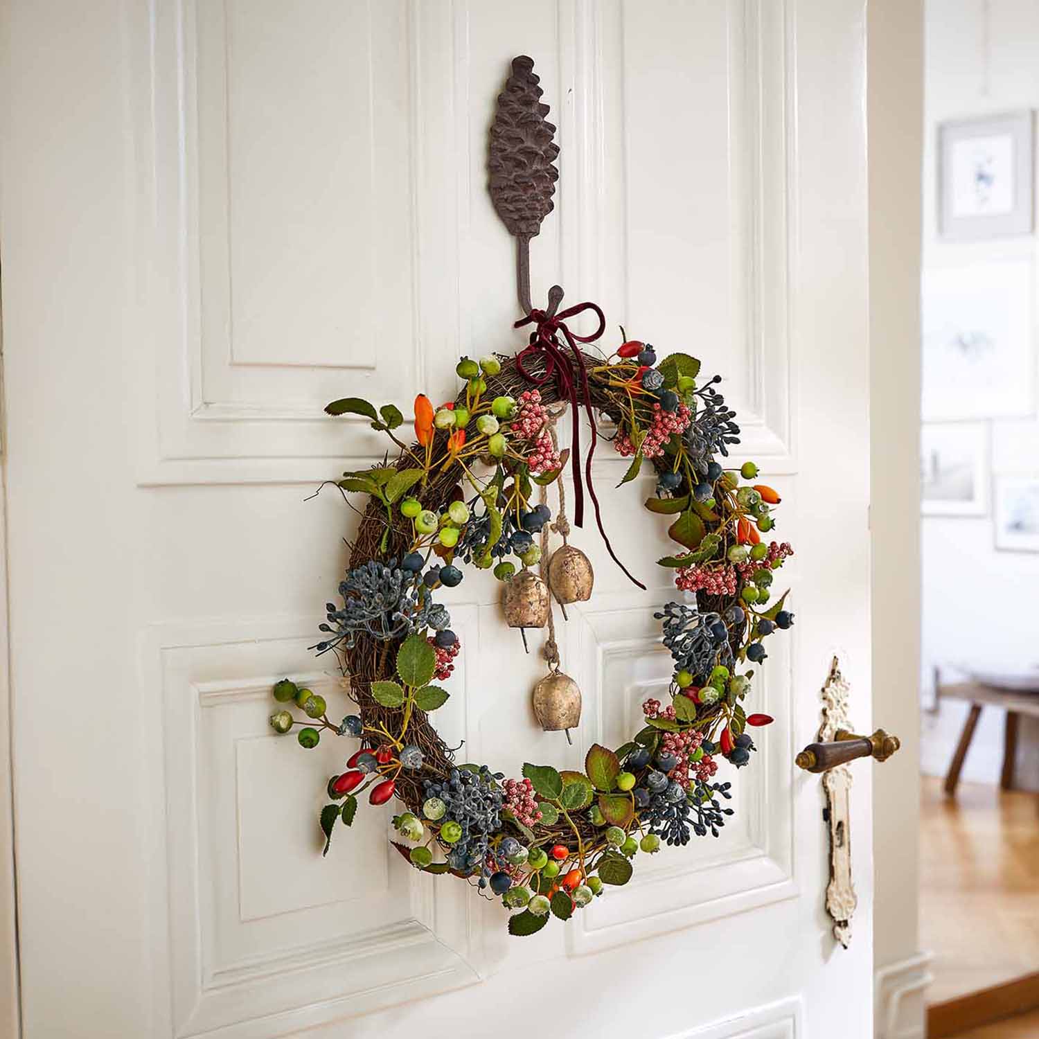 Decoratieve krans met gekleurde bessen en belletjes aan witte deur