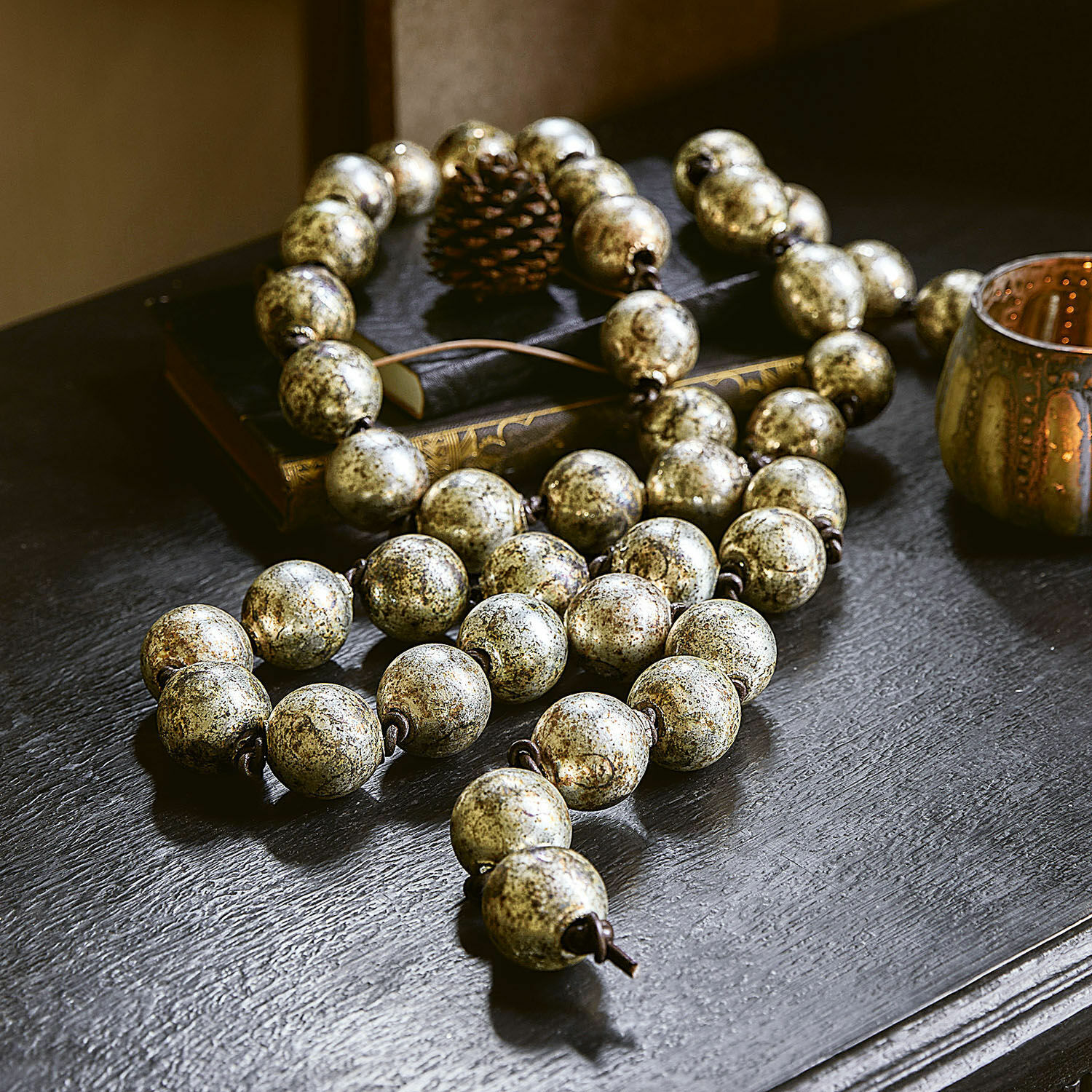 Guirlande Malou Decoratieve ketting met grote antiek-gouden kralen op zwarte tafel met boeken