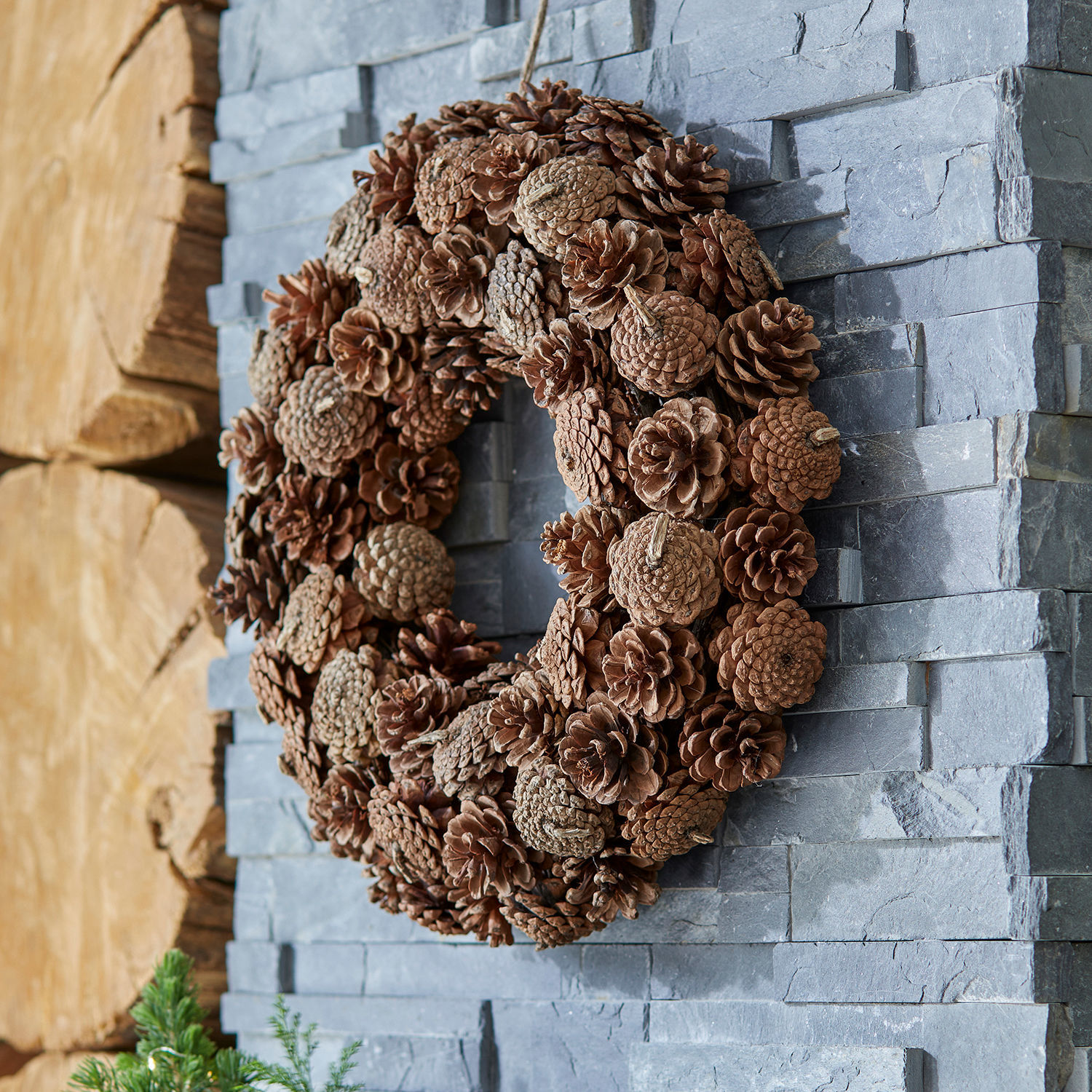 Krans Mellor Decoratieve krans van natuurlijke bruine dennenappels tegen een stenen muur