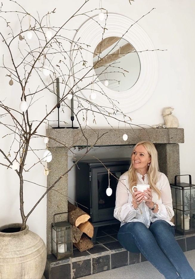 Vrouw zit bij stenen open haard met decoratieve takken en witte eieren in gezellige kamer