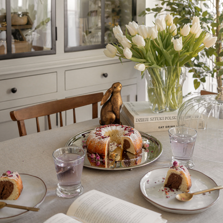 Tafel met marmercake op zilveren schaal, witte tulpen in glazen vaas en decoratief konijn