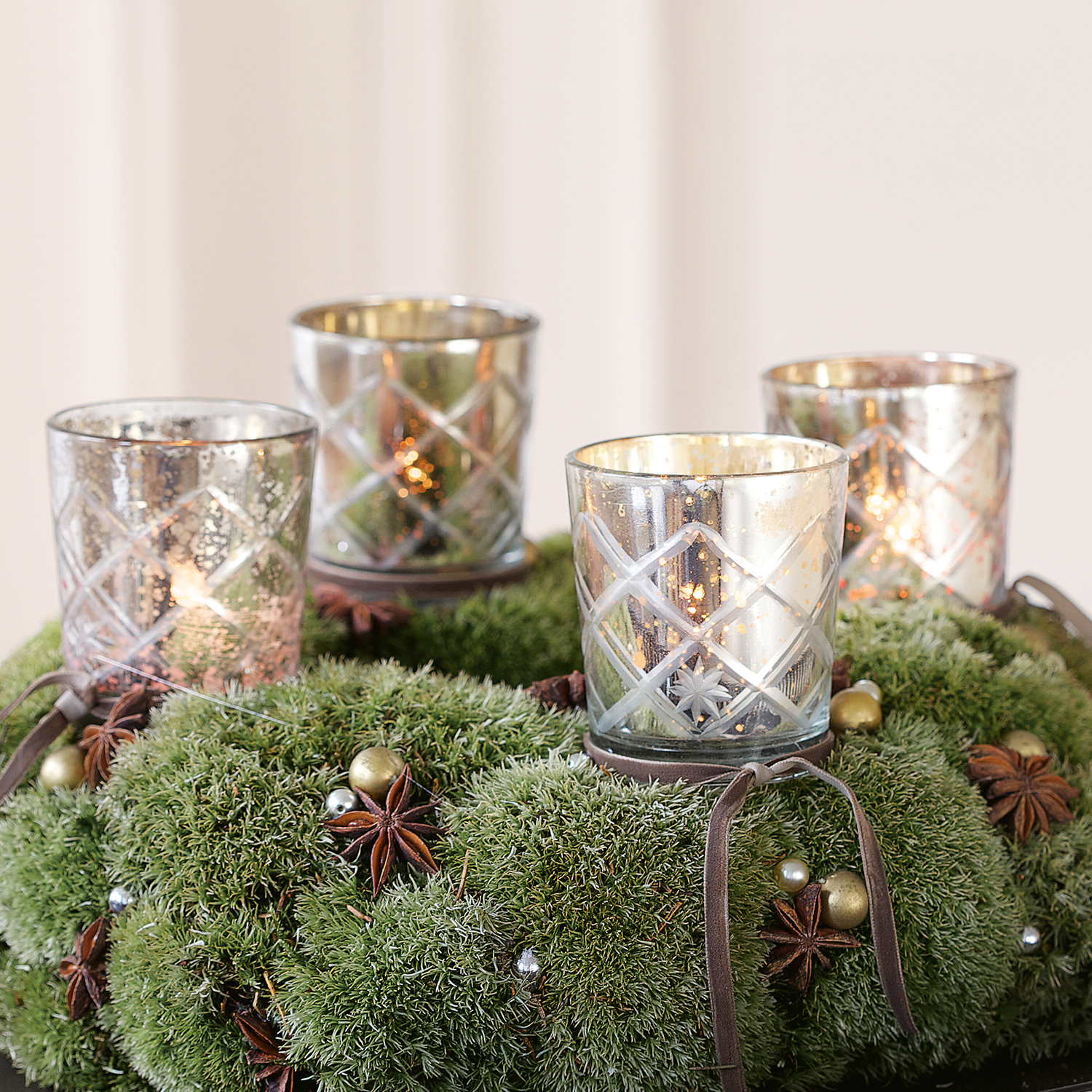 Glazen theelichthouders met ruitpatroon op groene moskrans met kerstdecoratie