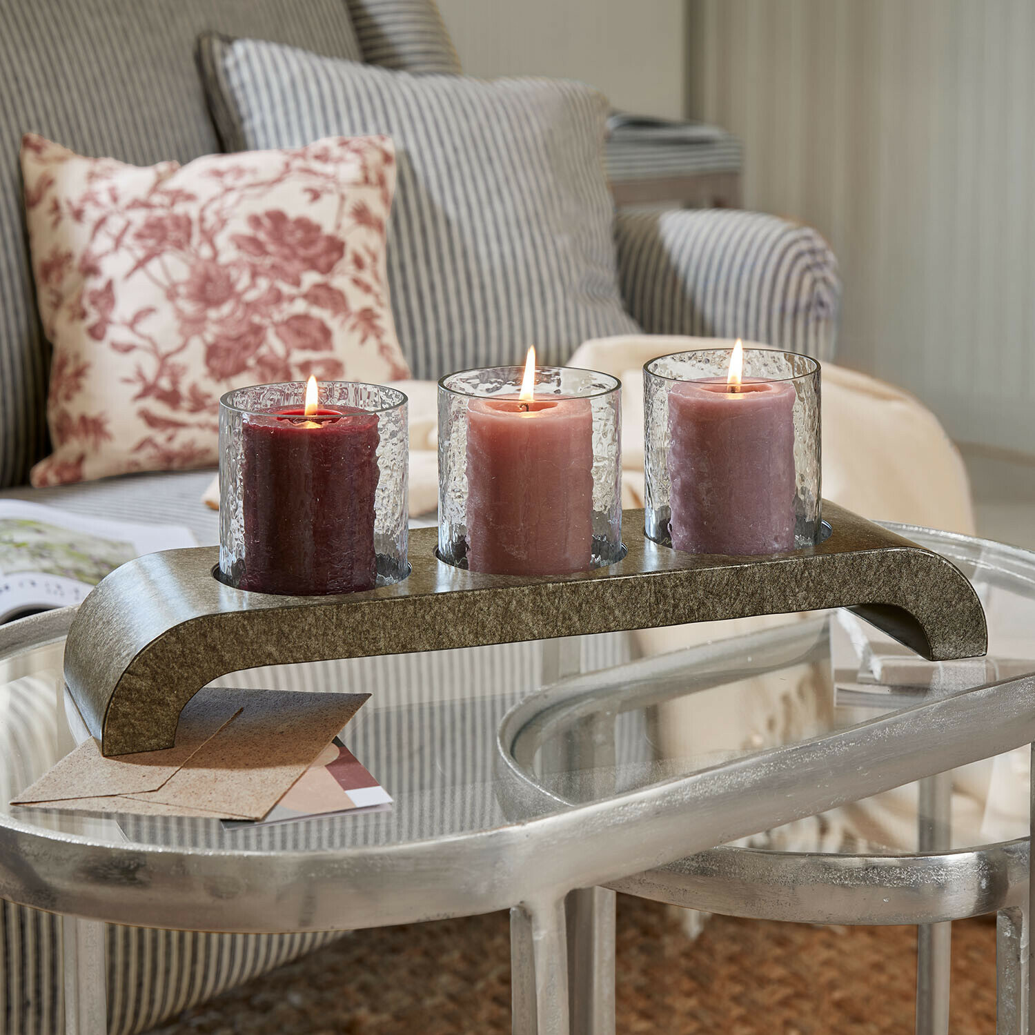 Drie brandende kaarsen in glazen houders op een metalen standaard op een glazen tafel in de woonkamer