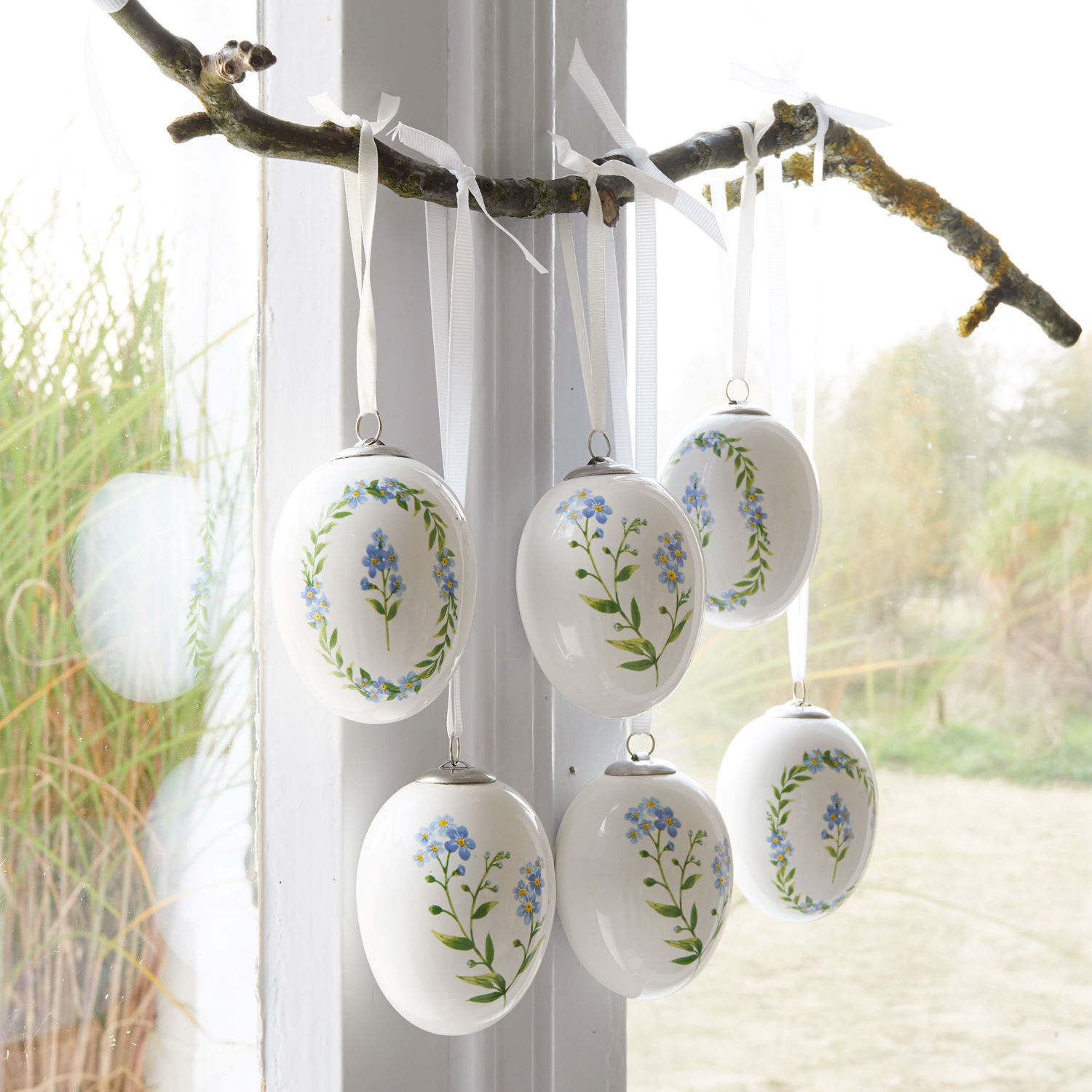 Paasei set van 6 Fierolla Witte keramische eieren met blauwe bloemen hangend aan tak bij raam, lentebloemdecoratie