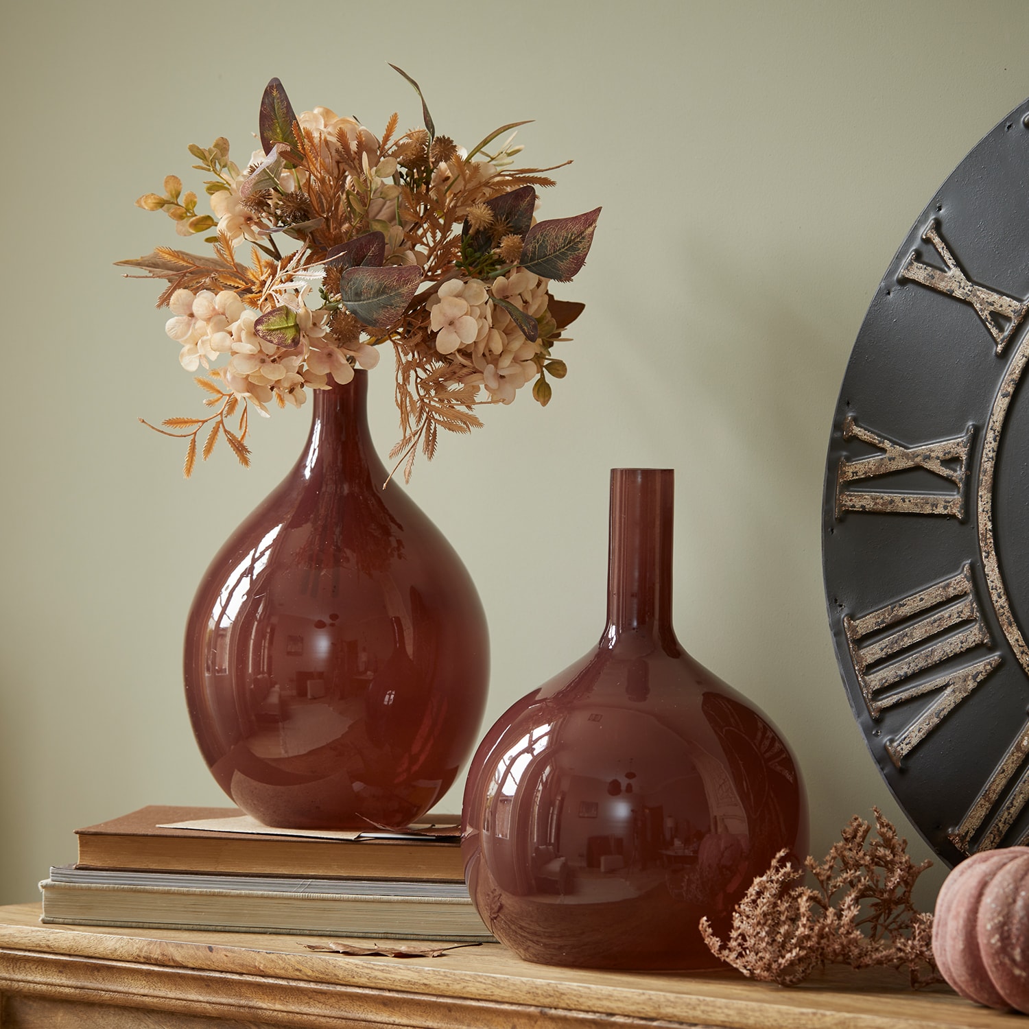 Twee bordeauxrode glazen vazen op houten tafel met gedroogde bloemen en boeken