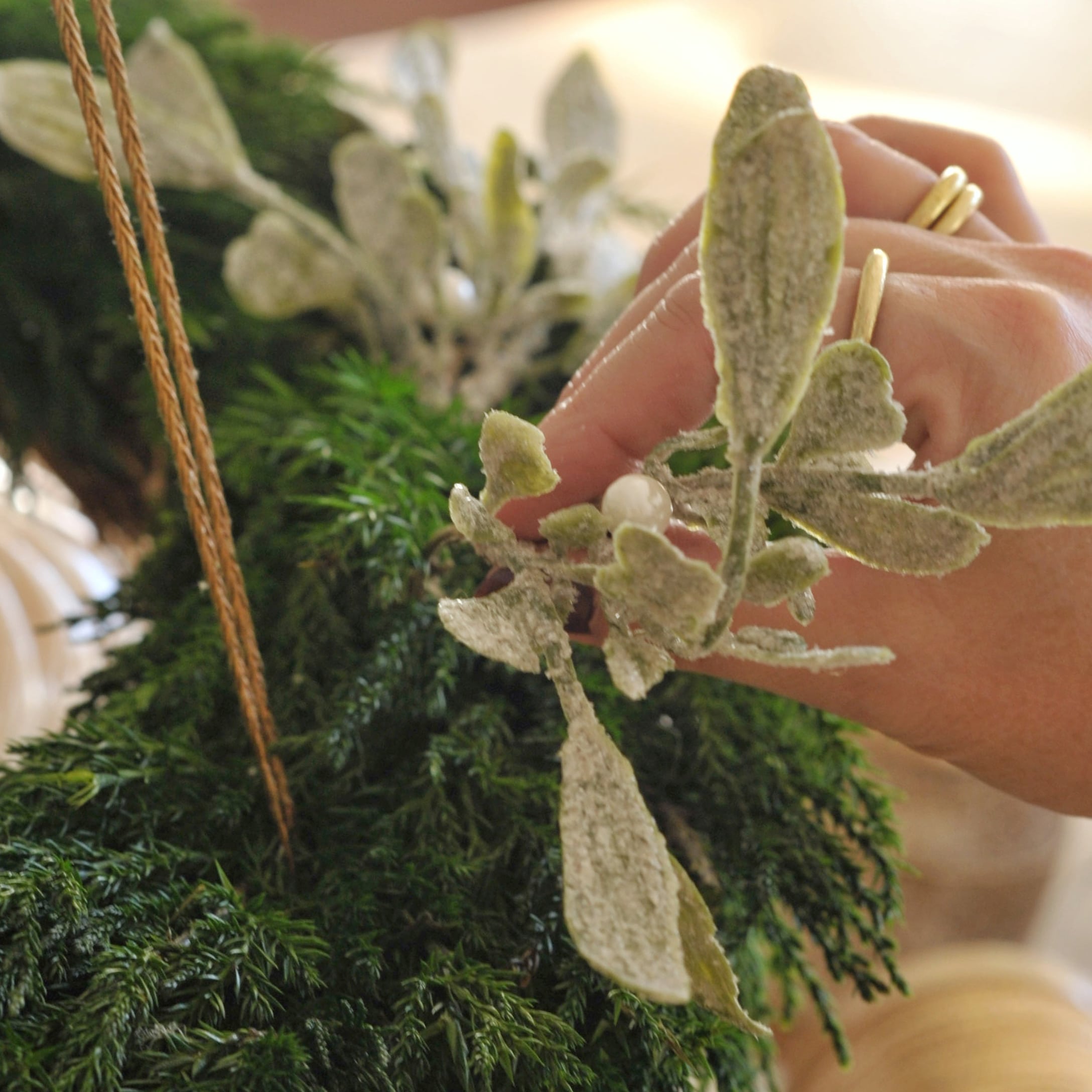 Hand die groene adventskrans versiert met witte bladeren en parelversieringen voor kerstdecoratie