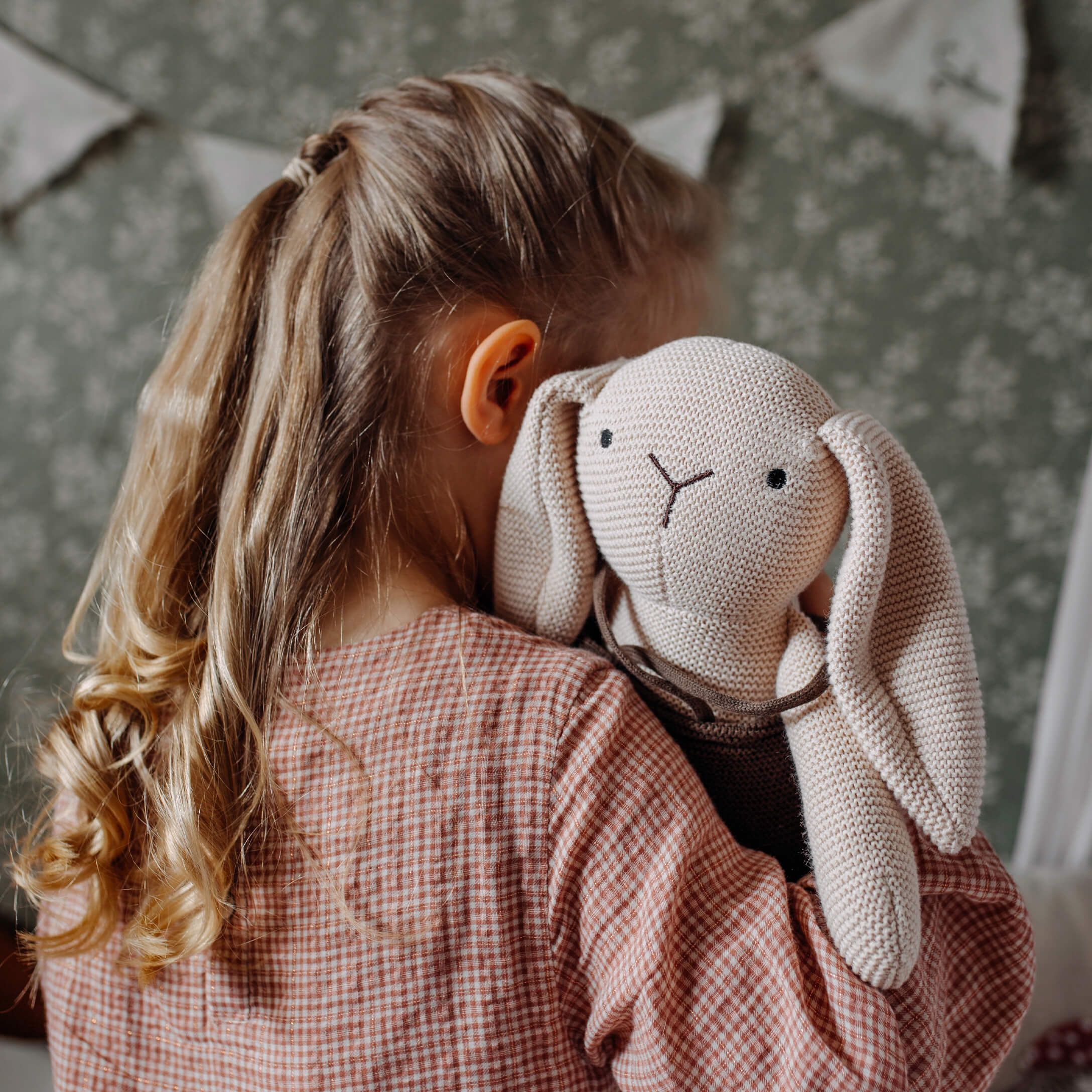 Meisje knuffelt beige gebreide knuffelkonijn in kinderkamer