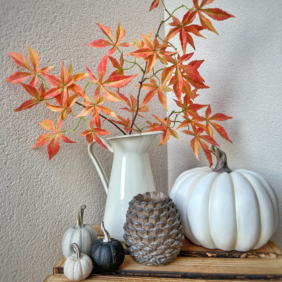 Witte decoratieve kan met oranje-rode bladeren en decoratieve pompoenen op houten plank