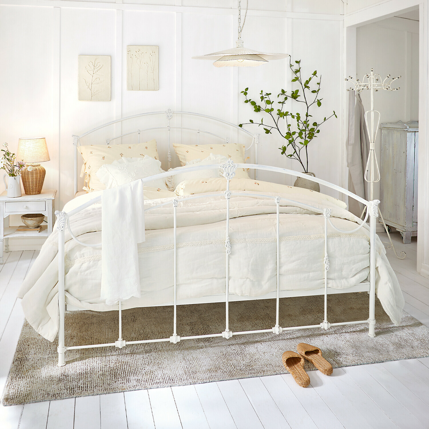 Witte metalen bedframe met crèmekleurig beddengoed en natuurlijke vloerkleed in lichte slaapkamer
