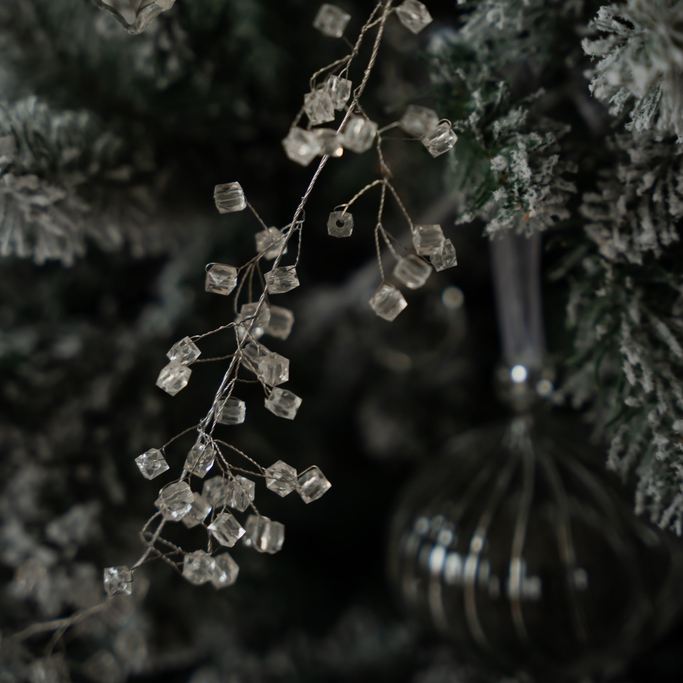 Decoratieve transparante kristallen aan draad tak tegen achtergrond van groene en witte kerstboom