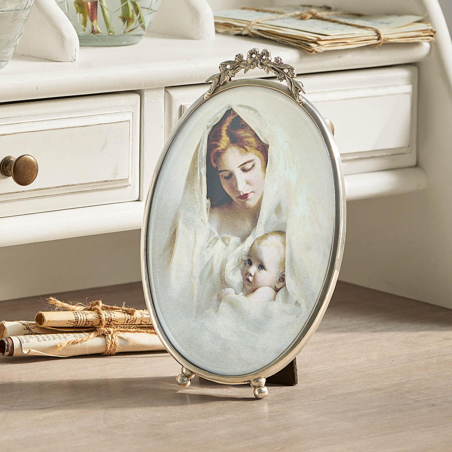 Ovale metalen fotolijst met versiering en afbeelding van moeder met baby in witte stof