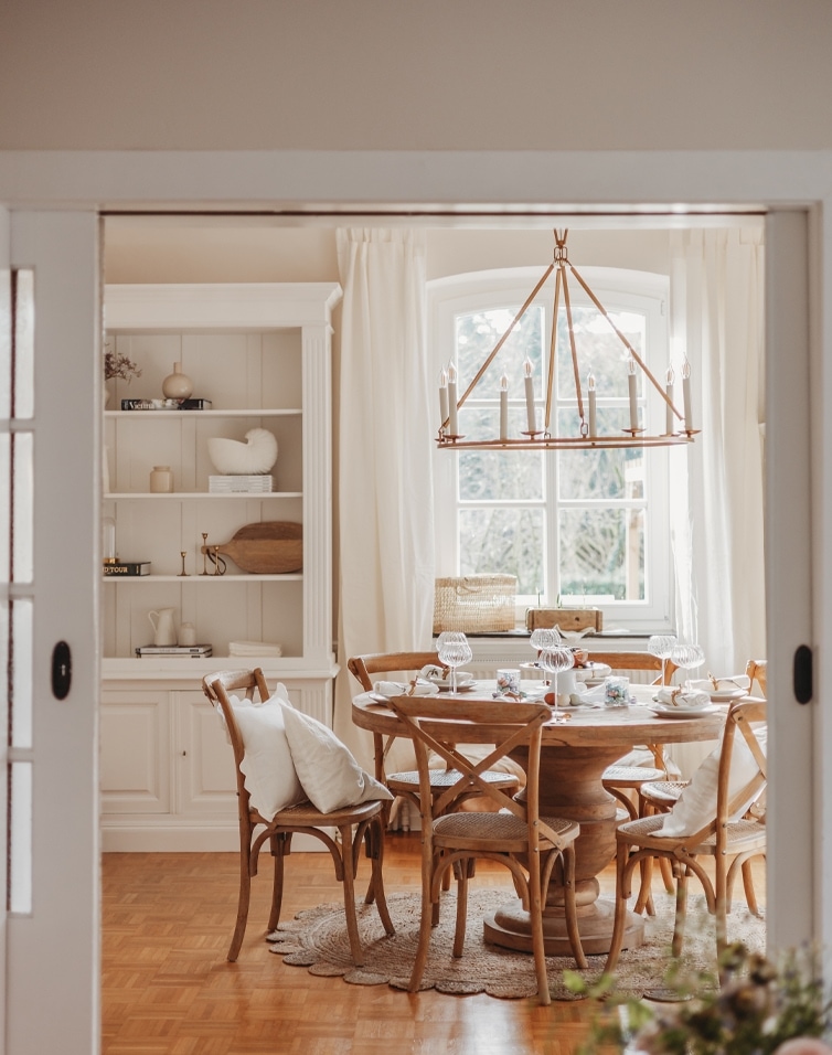 Eetkamer met ronde houten tafel, natuurlijke stoelen en een hangende kroonluchter met kaarsen