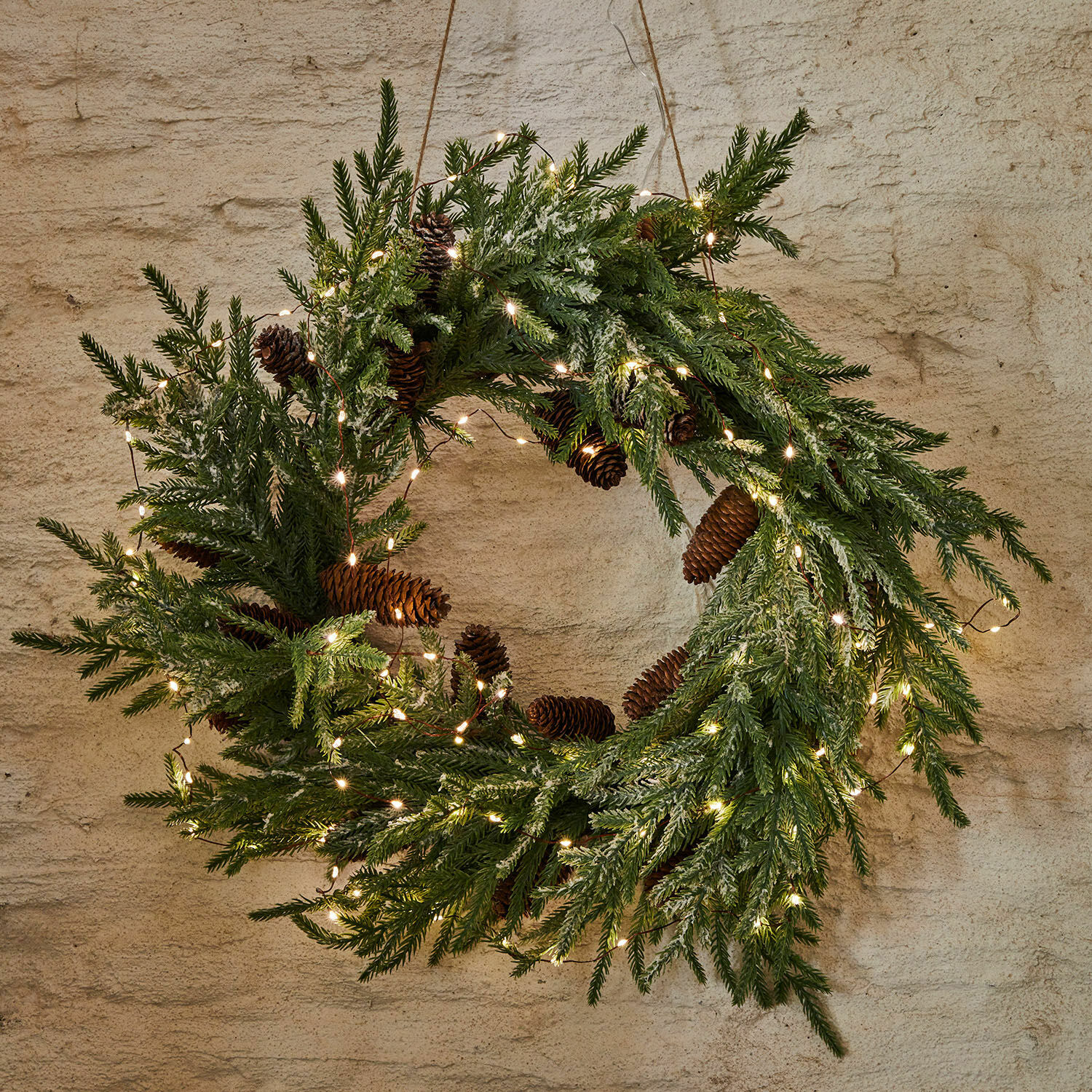 Kerstkrans van groene takken en dennenappels met LED-lichtjes aan de muur hangend