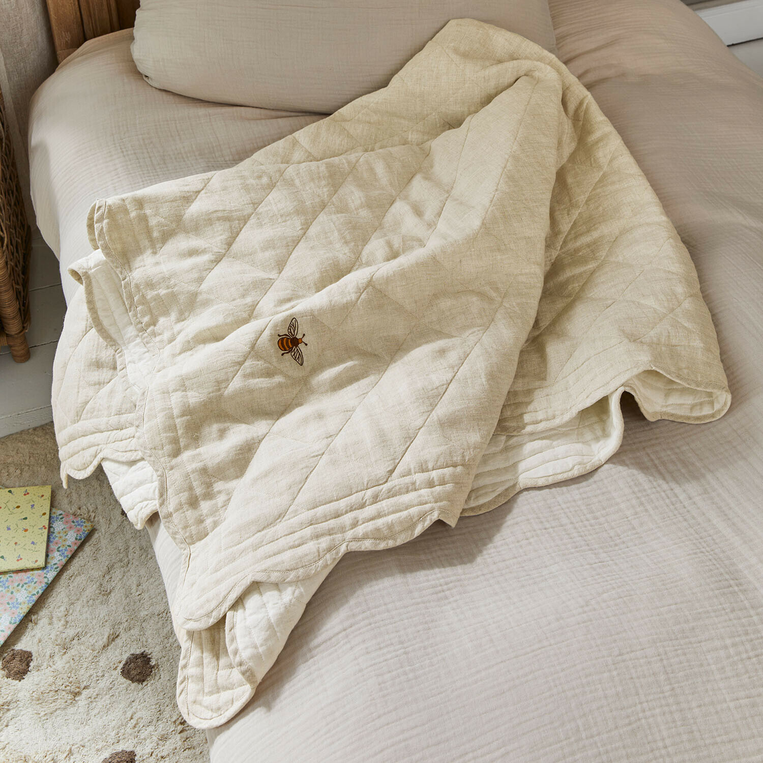 Beige doorgestikte deken met bijenborduursel op bed, zachte katoenen stof voor slaapkamer