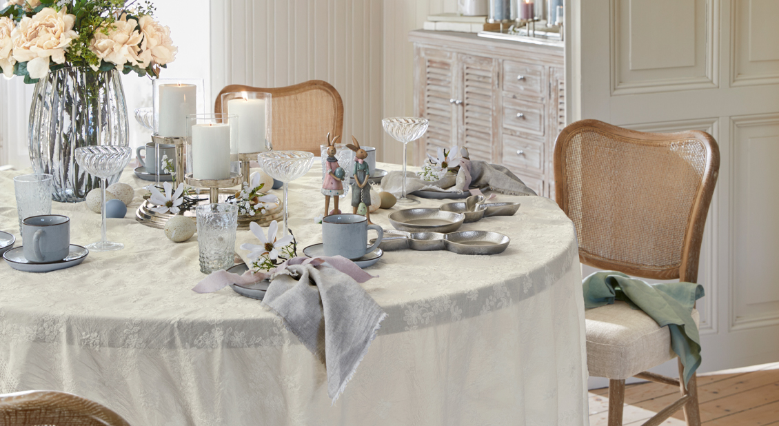 Fijn gedekte paastafel met crèmekleurig tafelkleed, kaarsen en elegant porseleinen servies