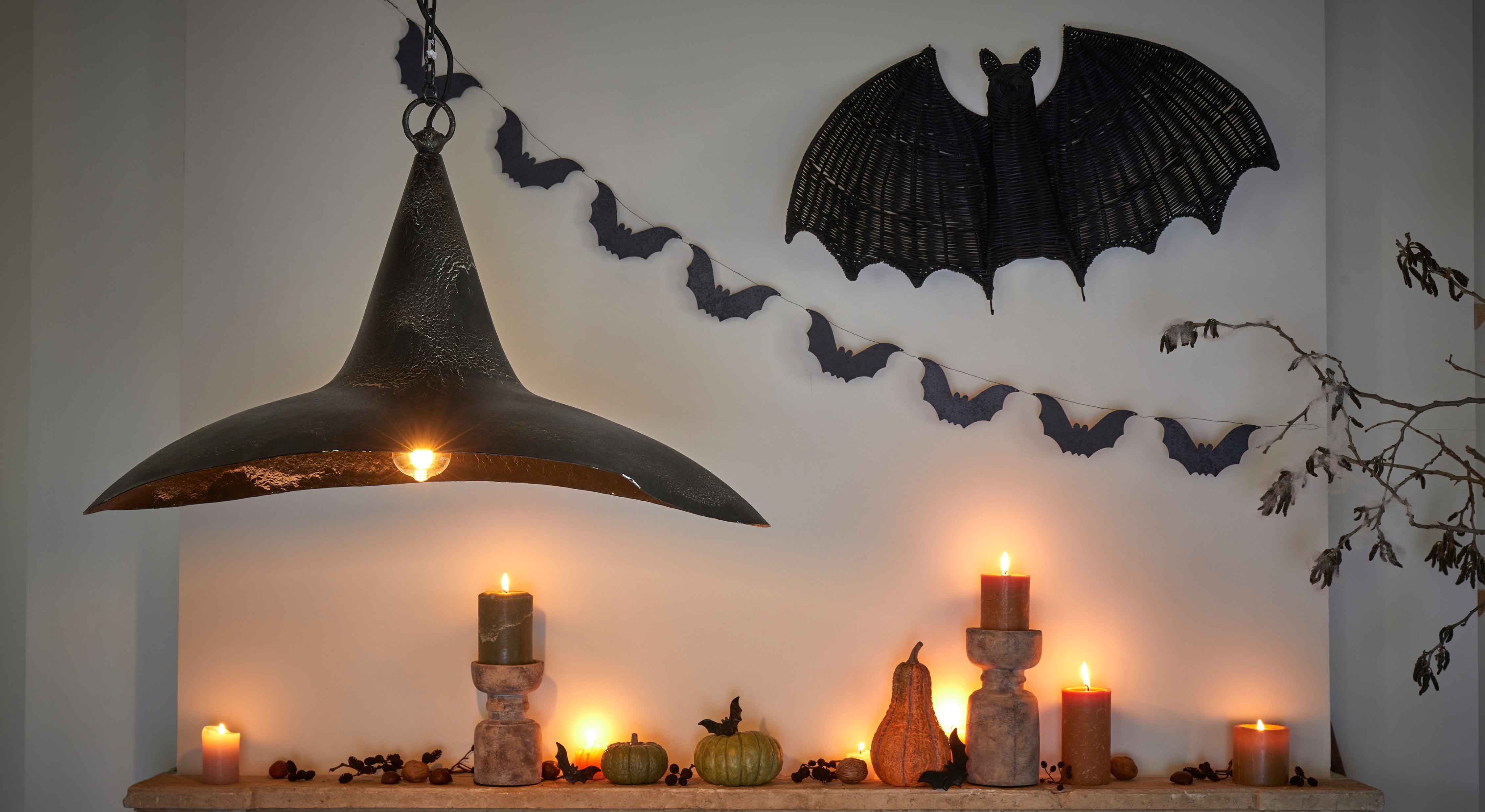 Halloweenversiering met zwarte kaarsen, pompoenen en zwarte metalen lamp aan muur met vleermuizen