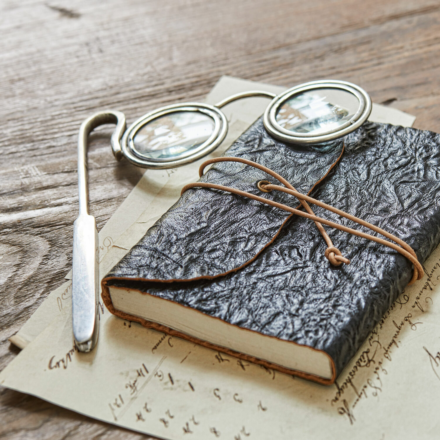 Loep Robert Zwart notitieboek van zacht leer met koordsluiting op houten tafel met bril en oude brieven