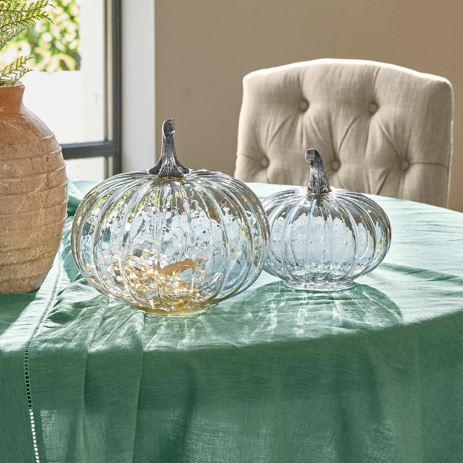 Transparante glazen decoratieve pompoenen met metalen stelen op groene tafelkleed voor interieurdecoratie