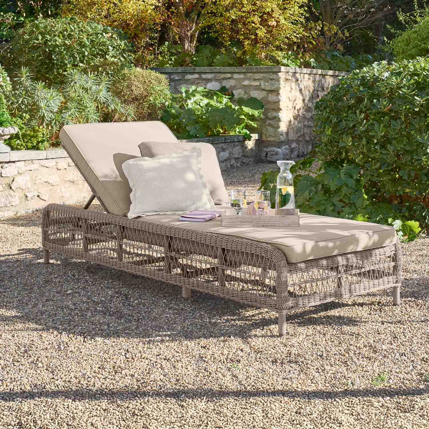 Beige tuinligstoel met kussen en gevlochten rieten frame op grind in groene tuin