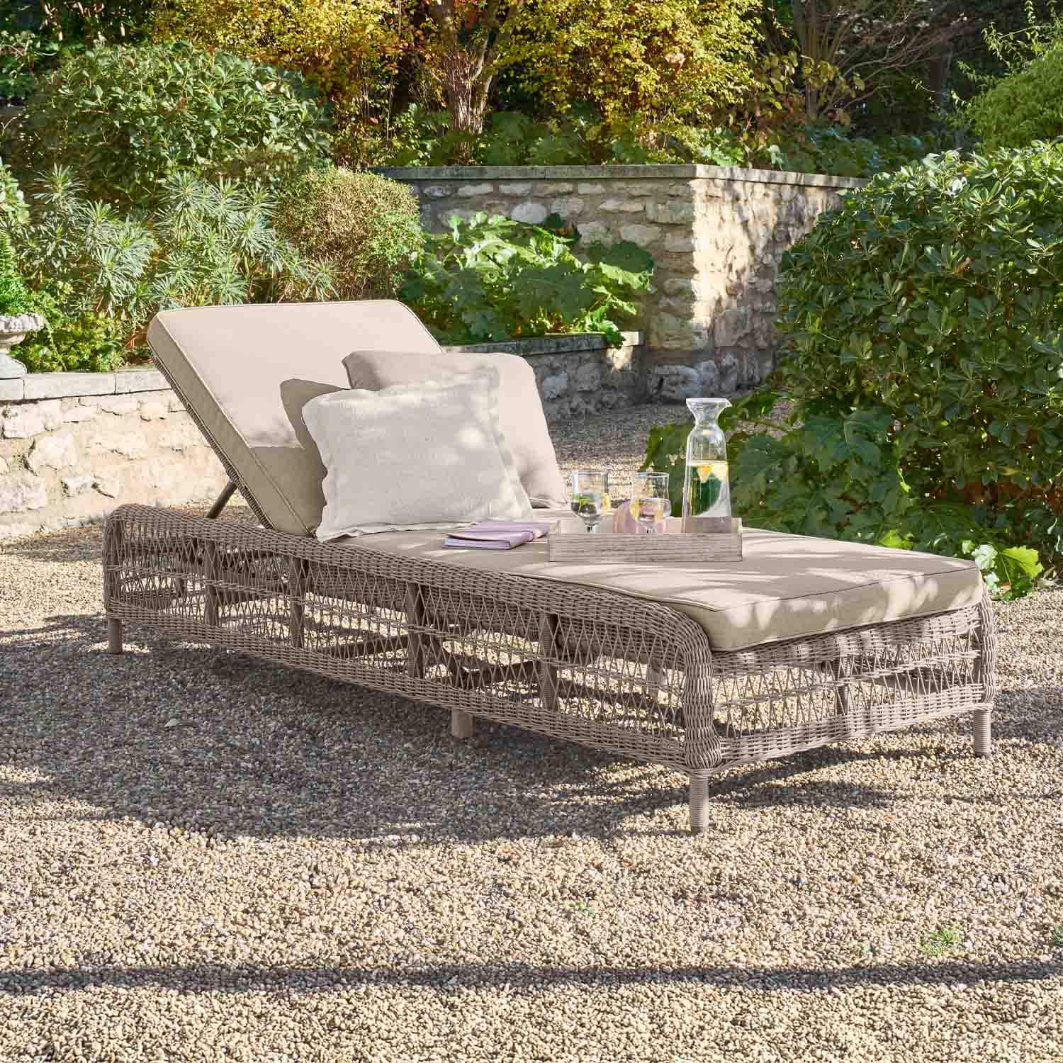 Beige tuinligstoel met kussen en gevlochten rieten frame op grind in groene tuin