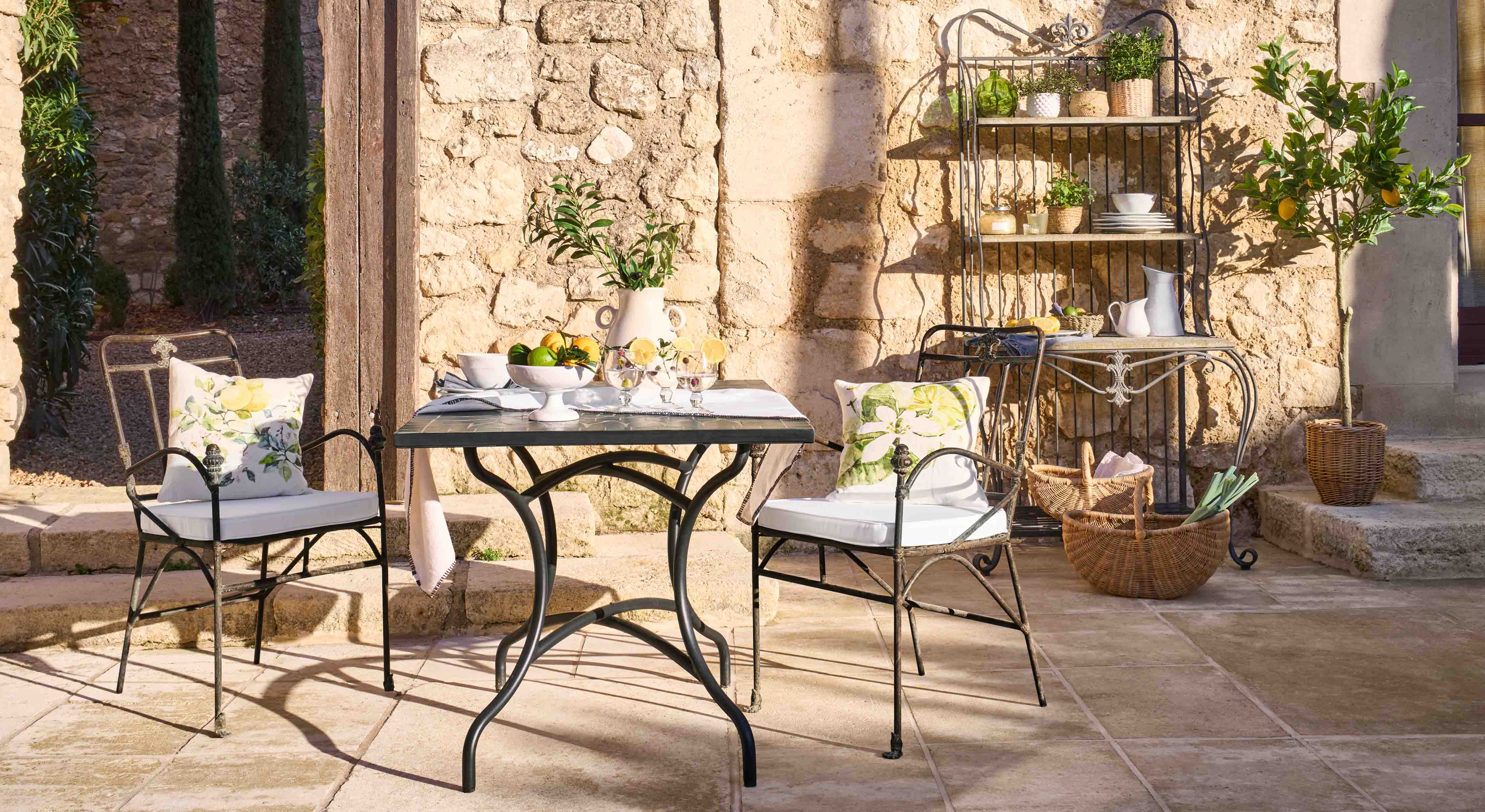 Metalen tafel en stoelen met bloemenkussens op stenen terras met tuindecoratie