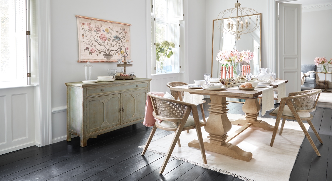 Lichte eetkamer met lichte houten tafel, rotan stoelen en subtiele bloemendecoratie in landelijke stijl