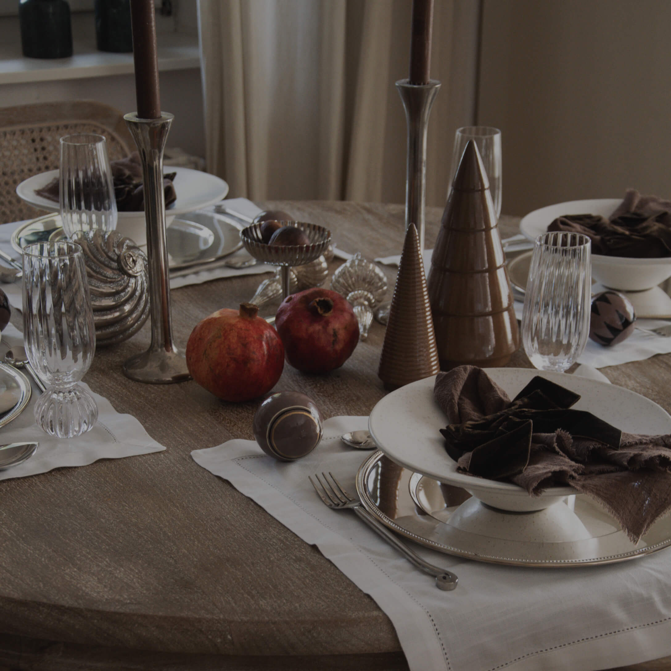 Stijlvol gedekte tafel met bruine keramische kegels, stoffen servetten en rode granaatappels