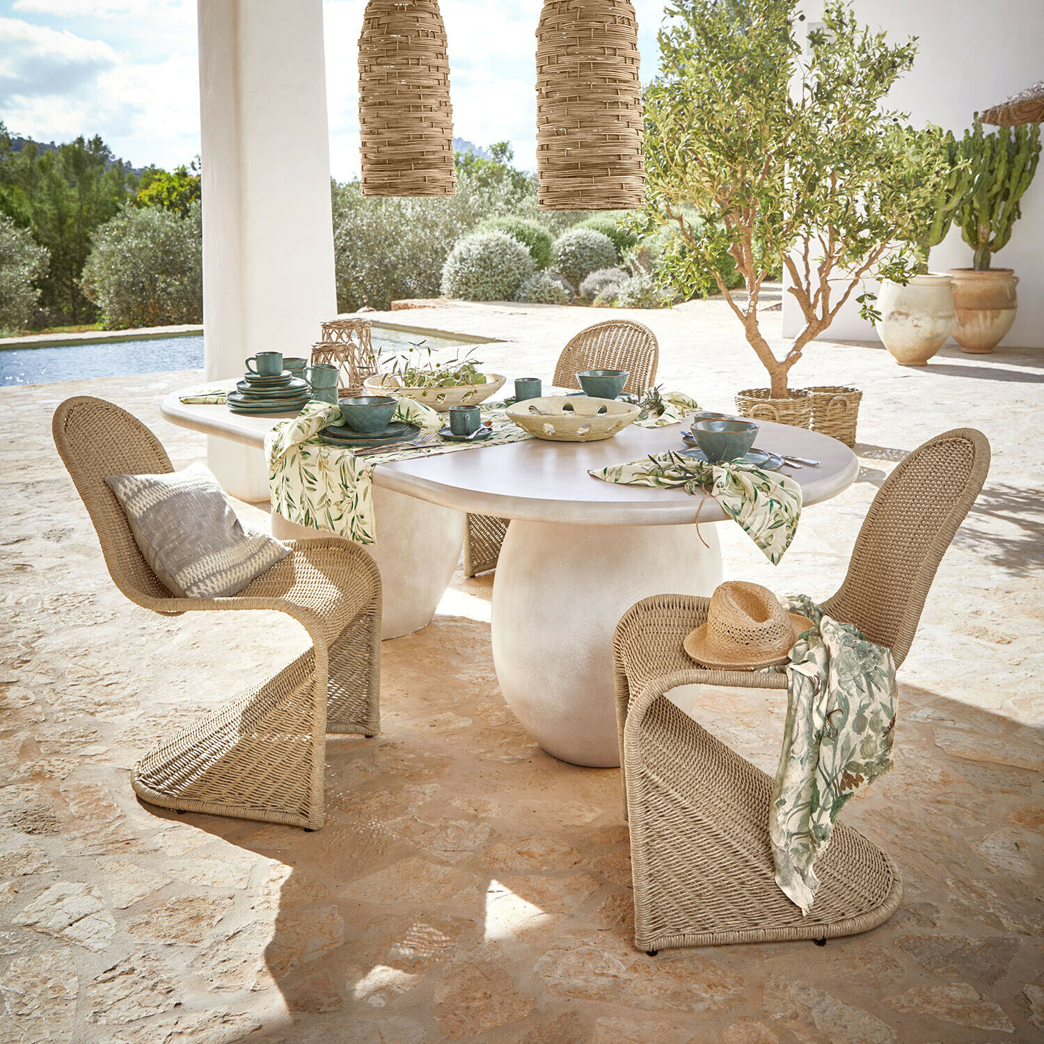 Ovale tafel met wit blad en natuurlijke rotan stoelen op terras met uitzicht op tuin
