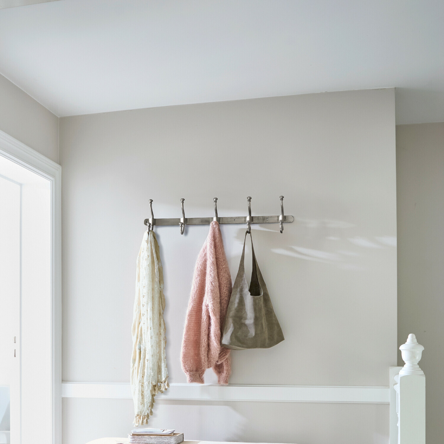 Metalen wandkapstok met vijf haken met roze trui, sjaal en tas eraan gehangen